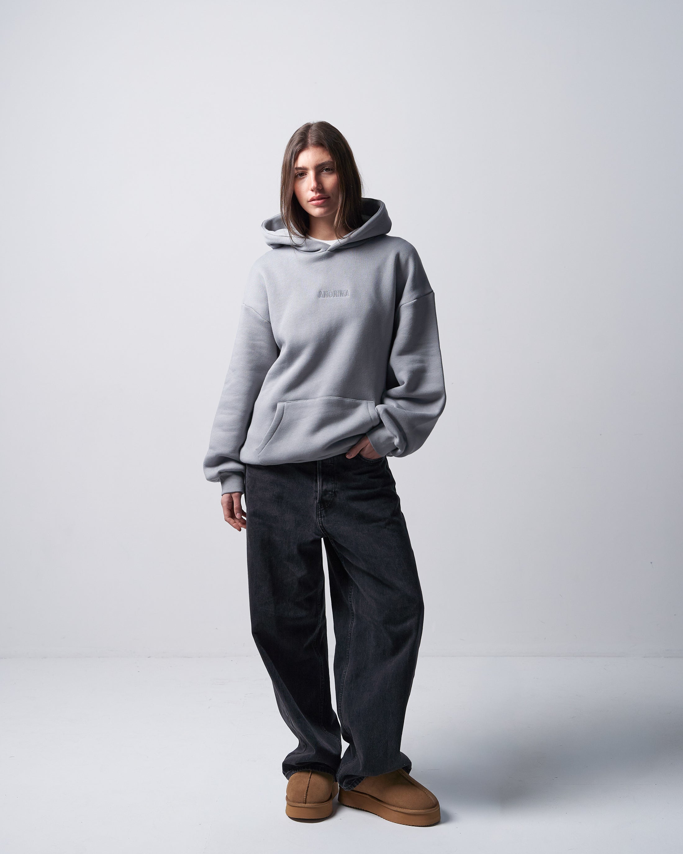 Person wearing a gray hoodie and dark jeans on a white background