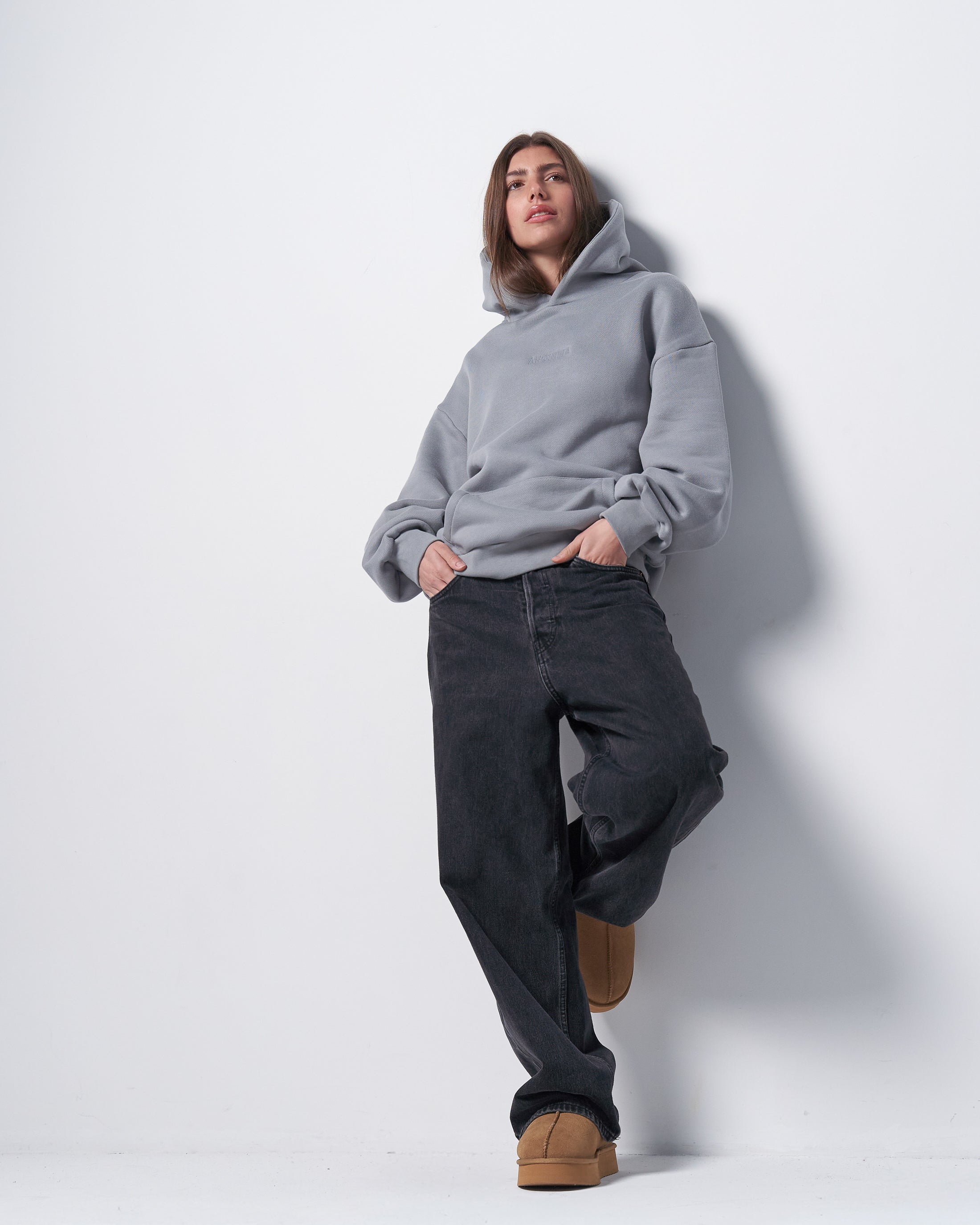Person wearing a gray hoodie and dark pants against a white background