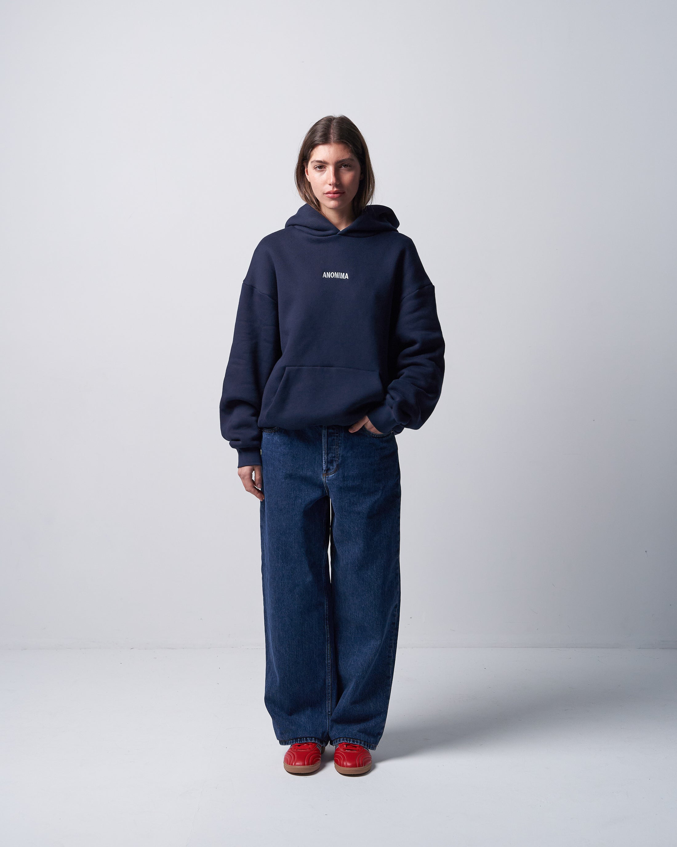 Person wearing a navy hoodie and jeans with a white logo on a light gray background