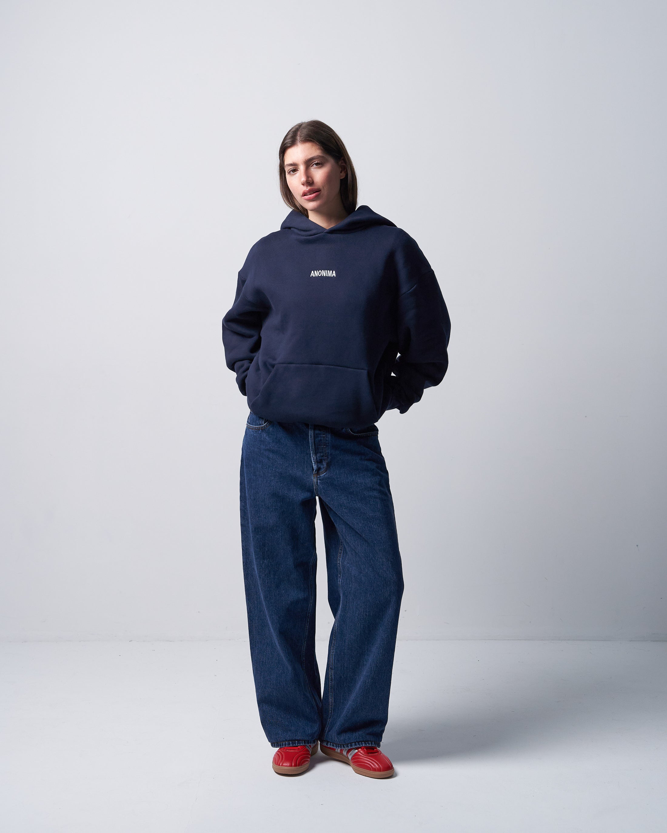 Person wearing a navy hoodie and jeans with red shoes on a white background