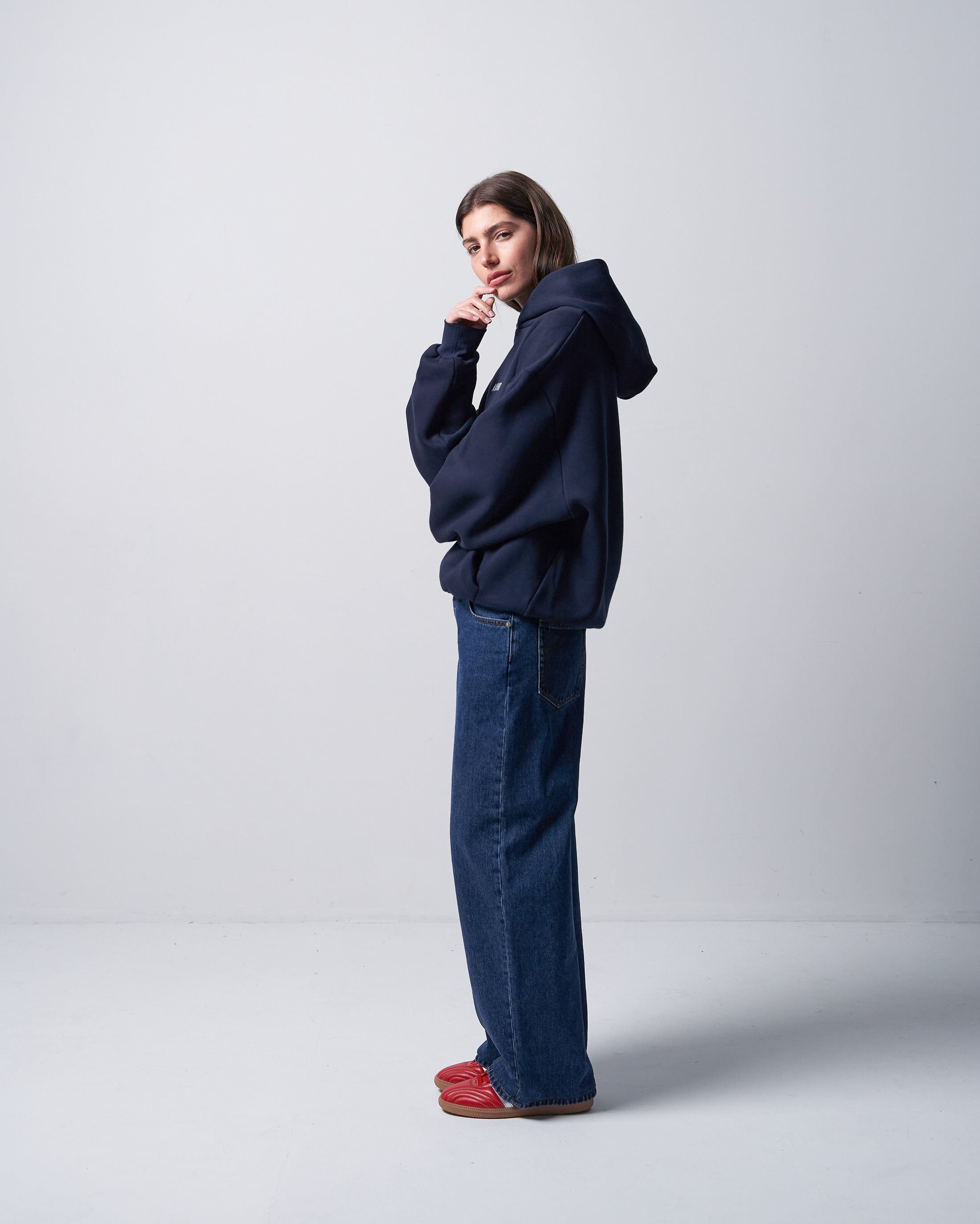 Person wearing a navy hoodie and jeans with red shoes on a white background