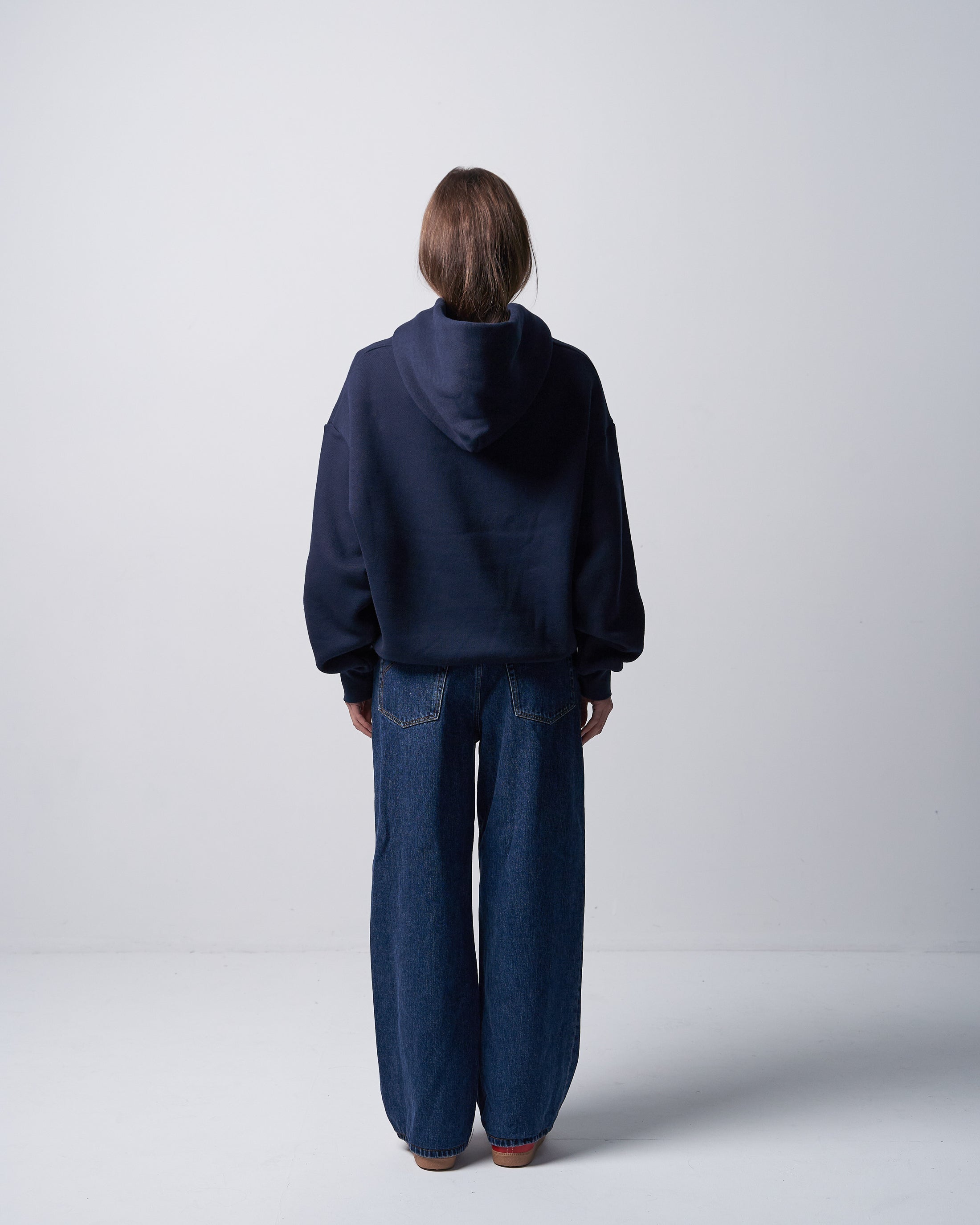 Person wearing a navy hoodie and jeans standing against a white background