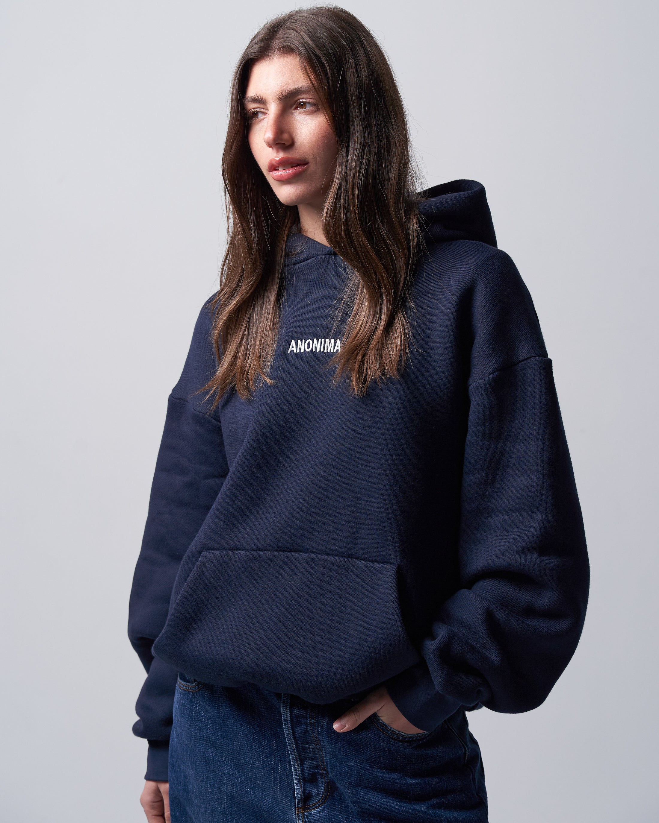 Person wearing a navy hoodie with 'ANONIMA' text on a light gray background