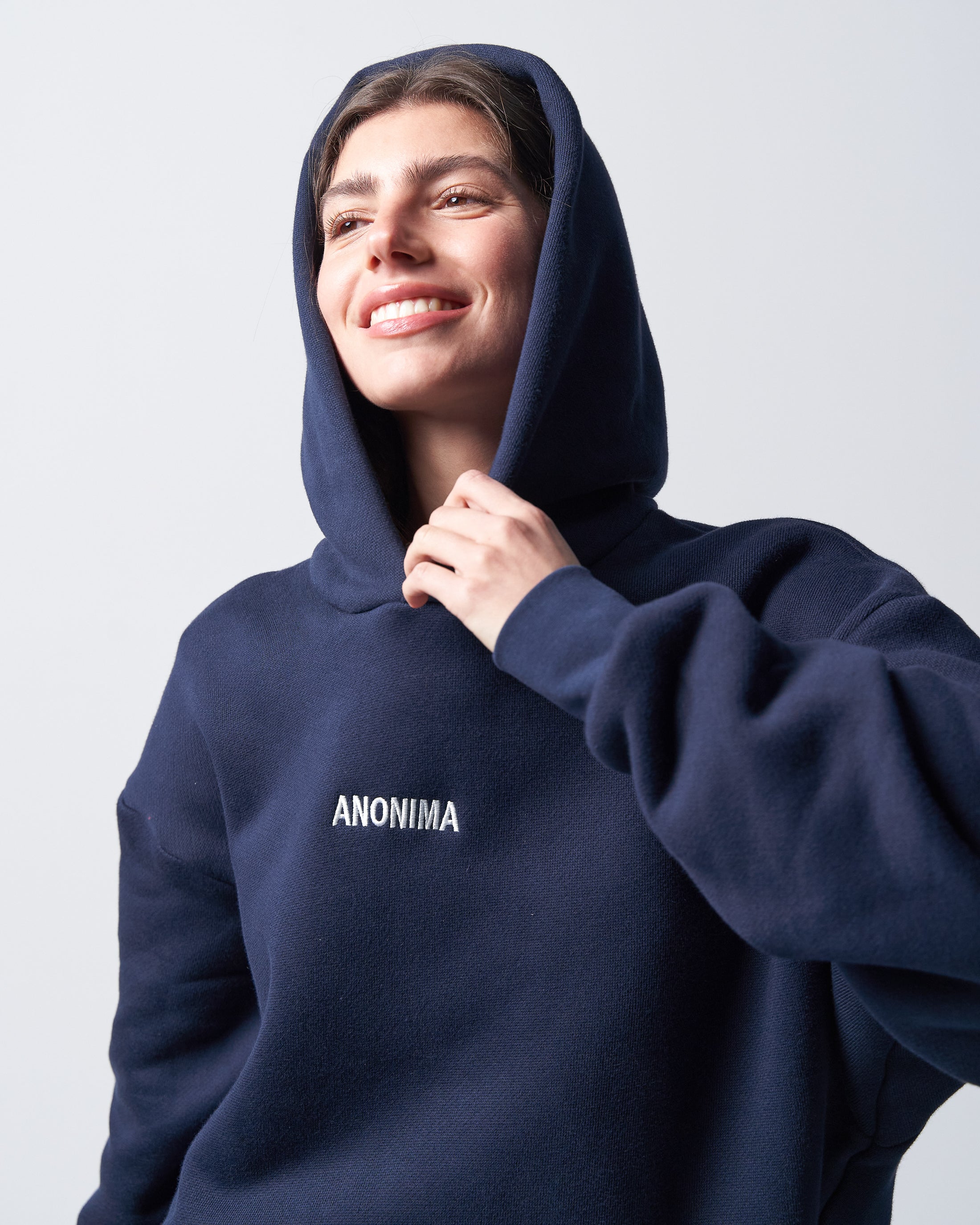 Person wearing a navy blue hoodie with 'ANONIMA' logo on a light gray background