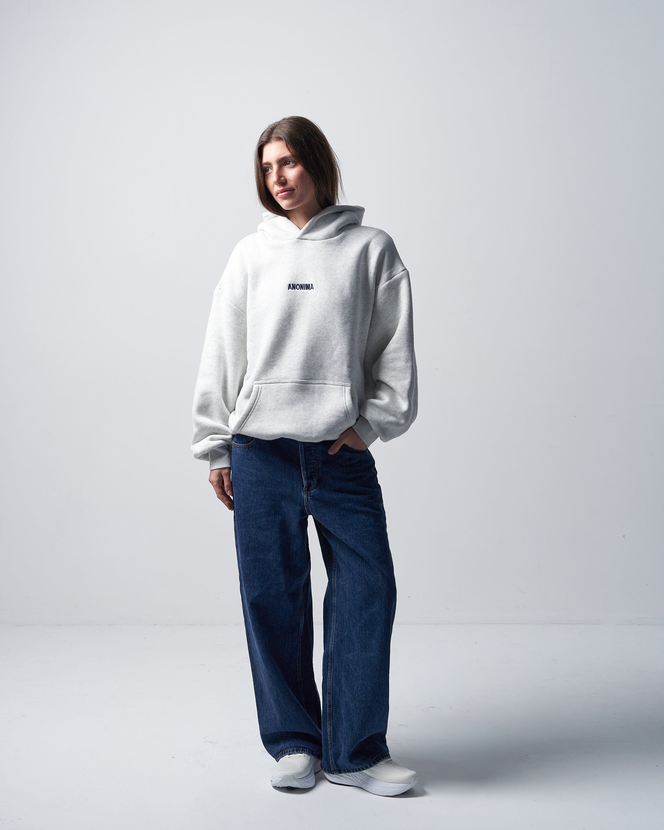 Person wearing a white hoodie and blue jeans on a light gray background