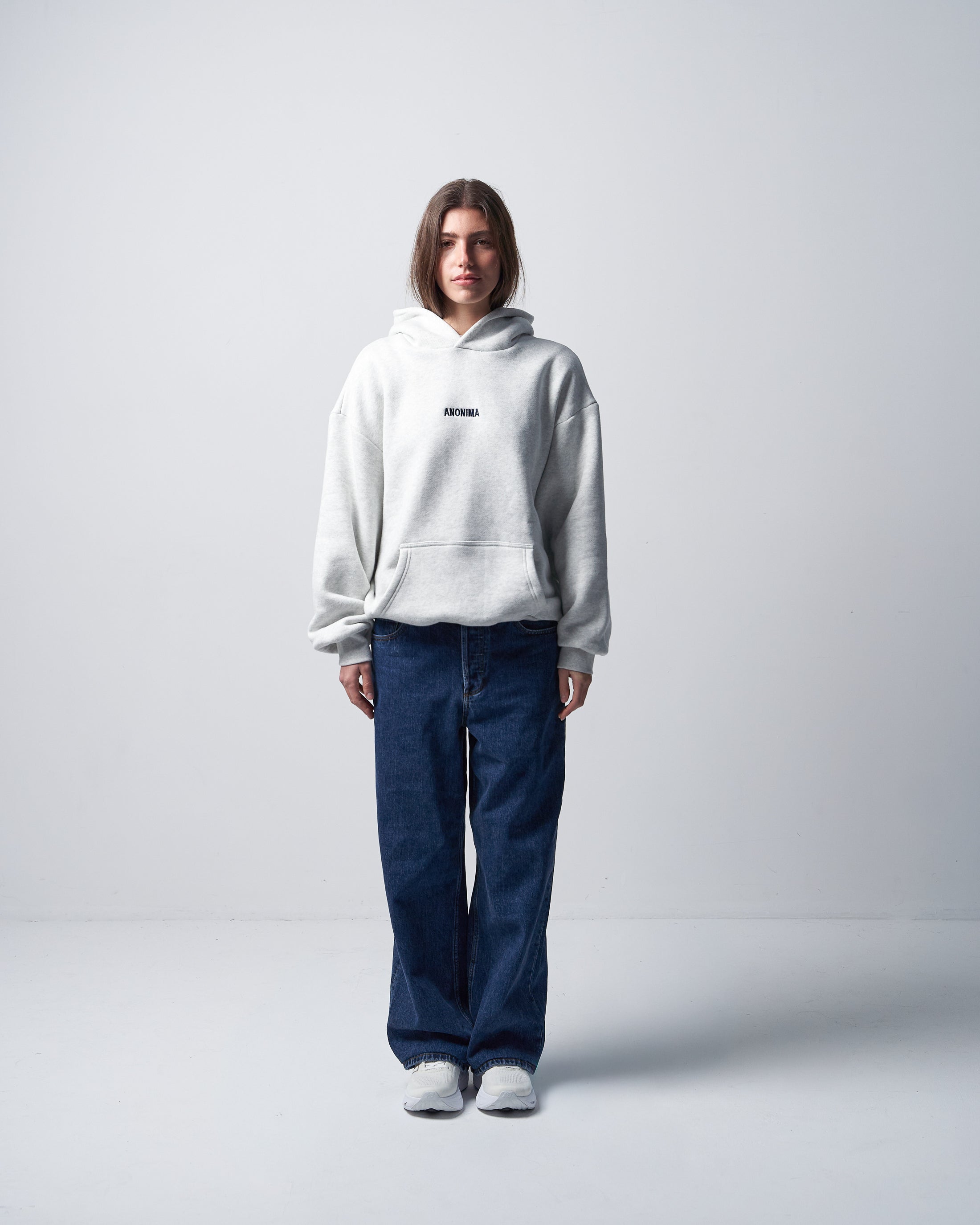 Woman wearing an ANONIMA heather grey hoodie against a white background