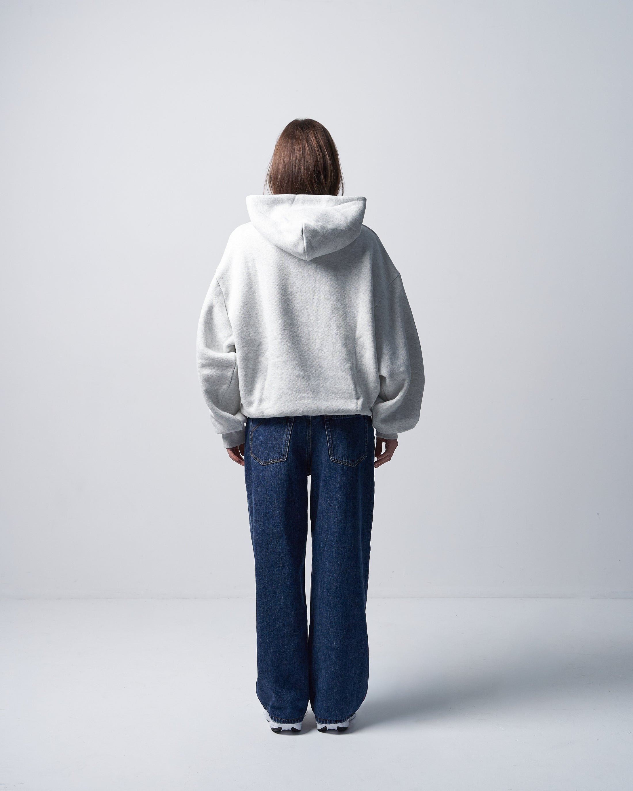 Person wearing a gray hoodie and blue jeans standing against a white background