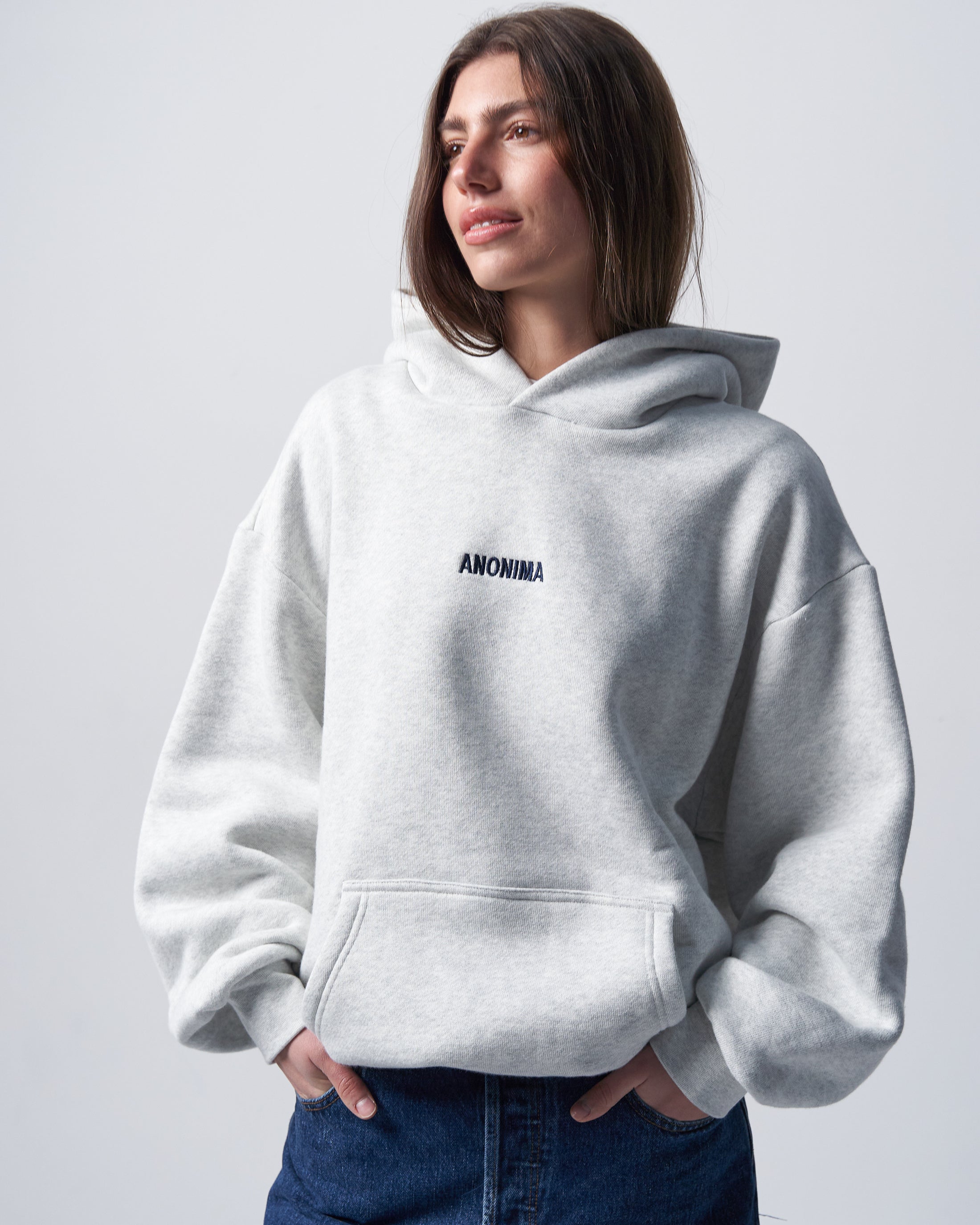 Person wearing a light gray hoodie with 'ANONIMA' text on a plain background
