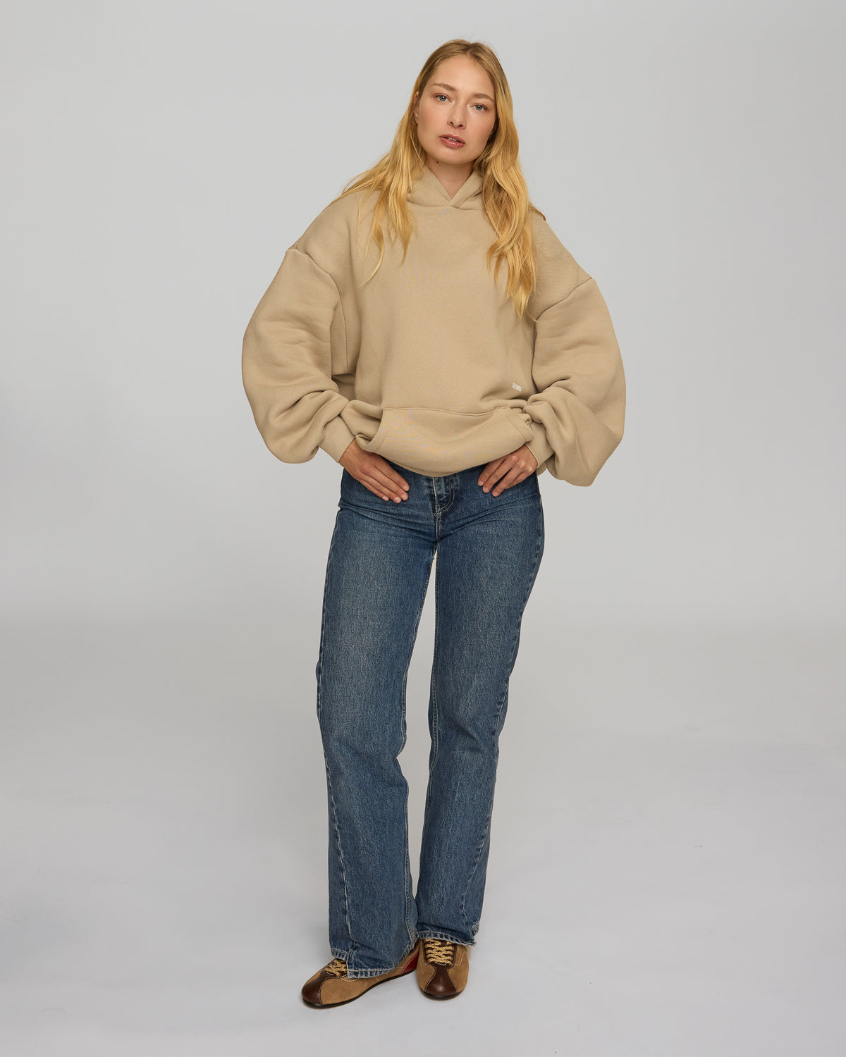 Woman wearing a beige sweater and blue jeans against a plain background