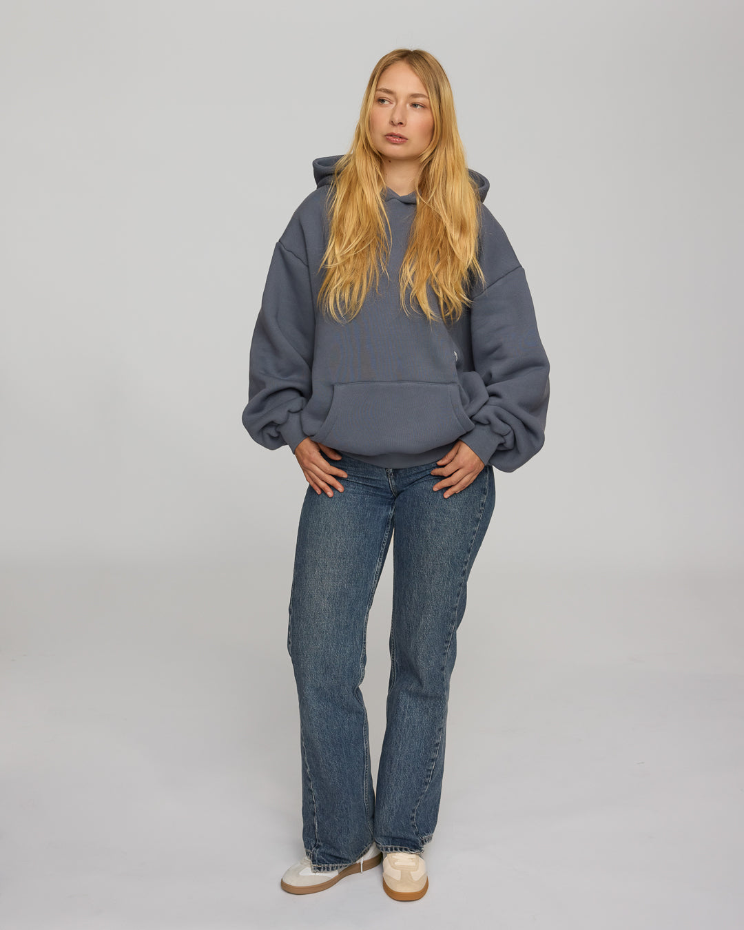 Person wearing a dusty blue hoodie and blue jeans on a plain background