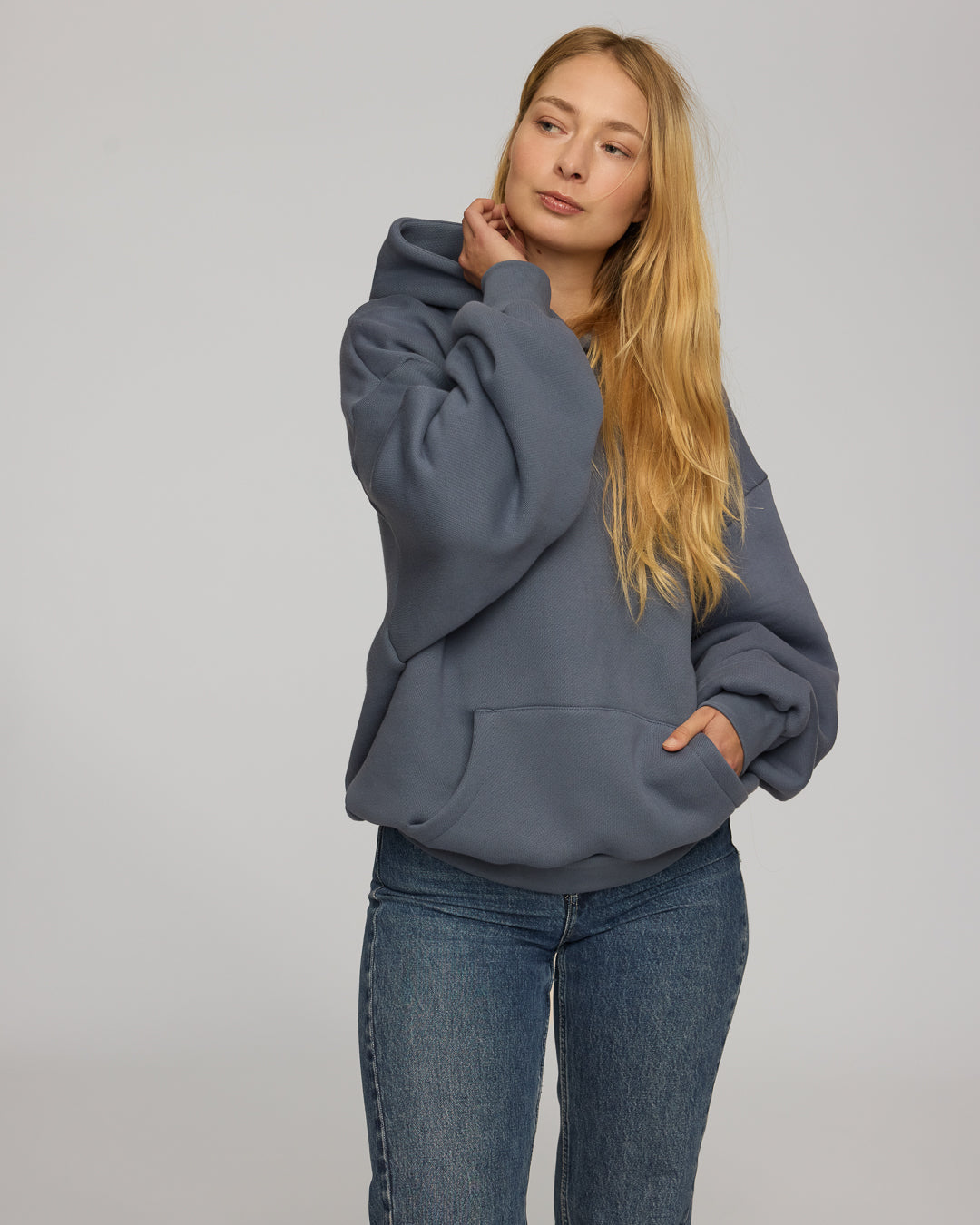Woman wearing a dusty blue hoodie and blue jeans on a plain background