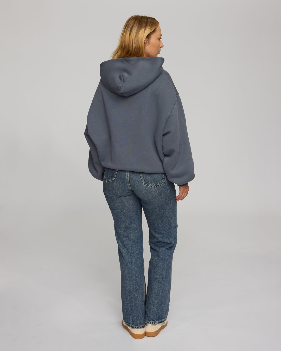 Person wearing a dusty blue hoodie and blue jeans from behind on a plain background
