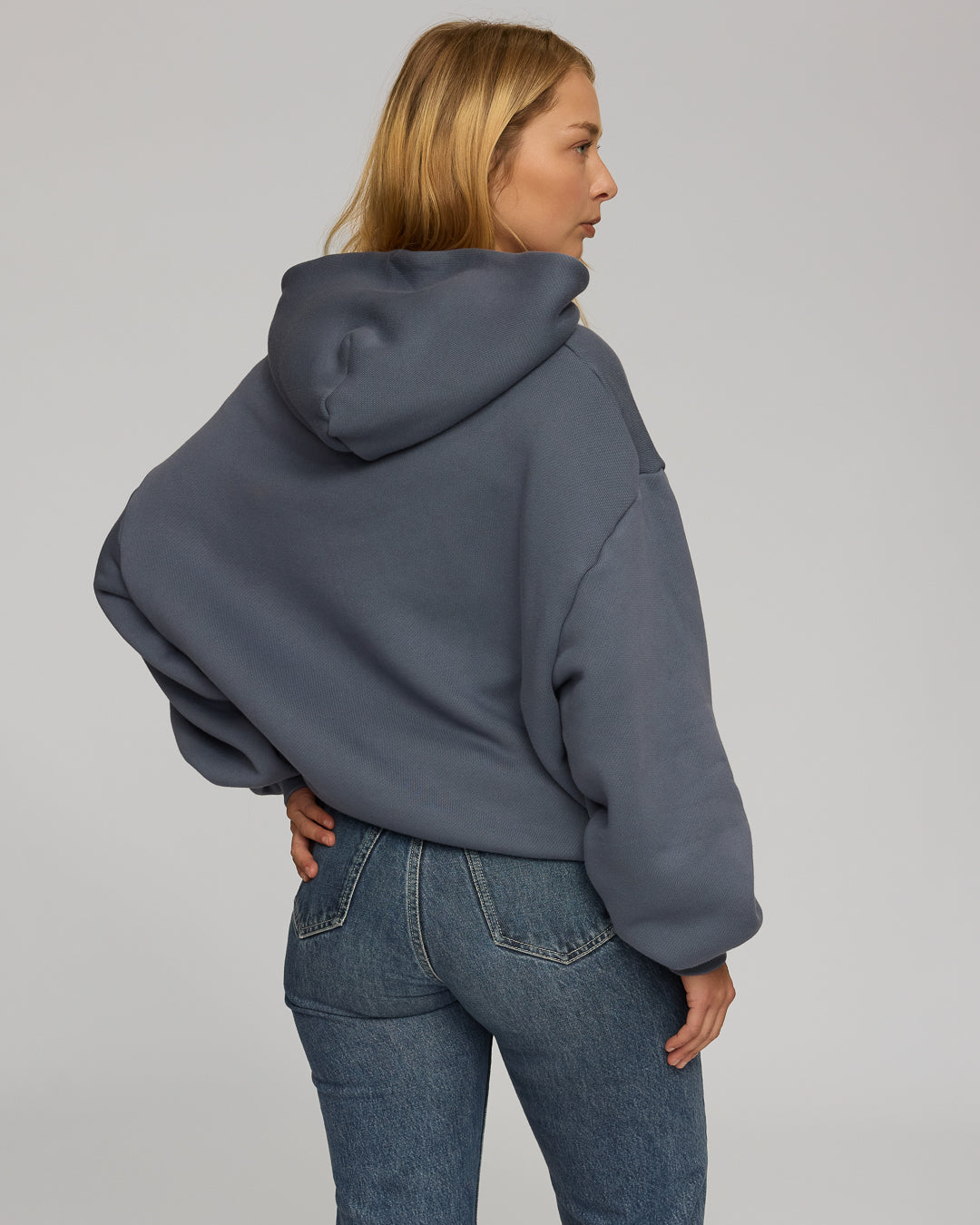 Person wearing a dusty blue hoodie and blue jeans on a plain background
