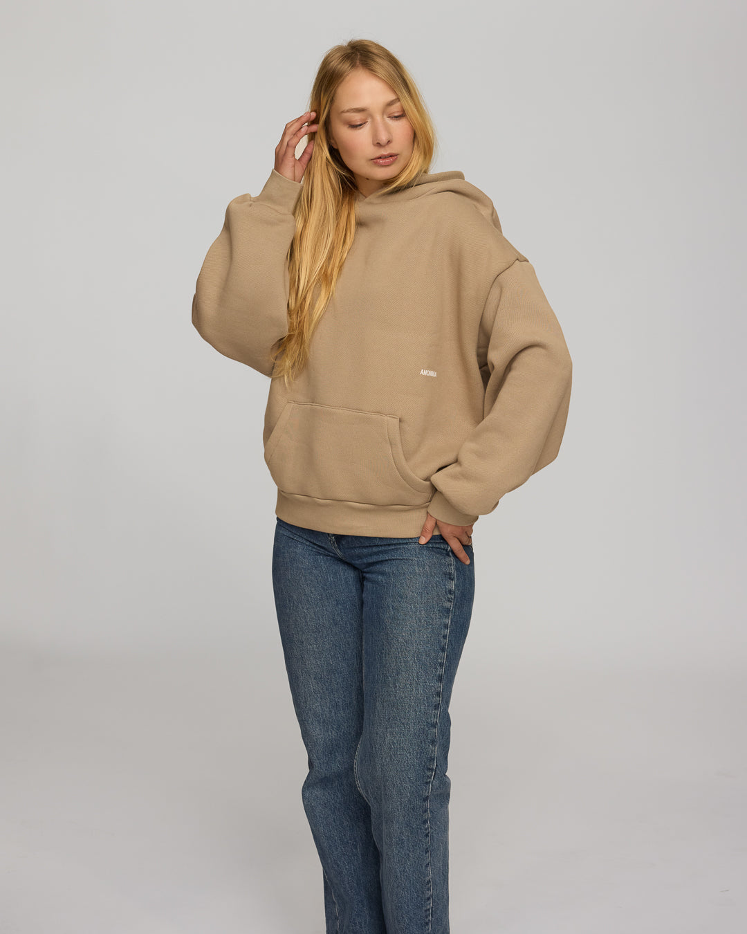 Woman wearing a coffee hoodie and blue jeans on a plain background