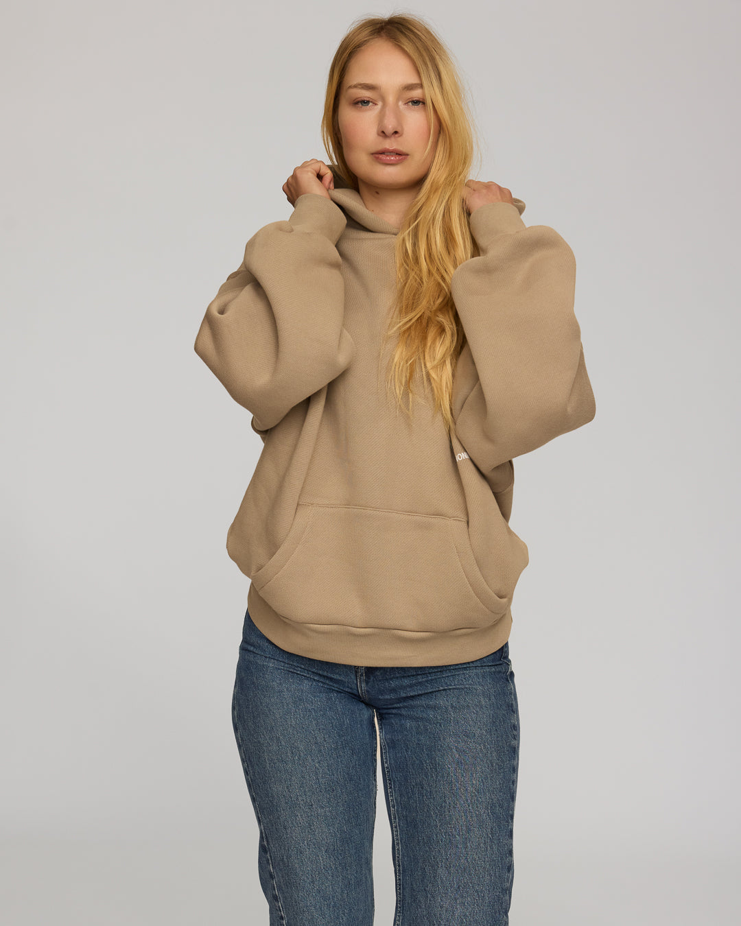 Woman wearing a coffee hoodie and blue jeans on a plain background