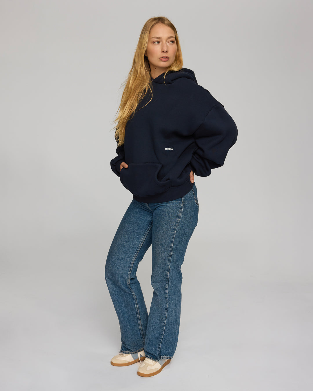 Woman wearing a navy hoodie and blue jeans on a gray background