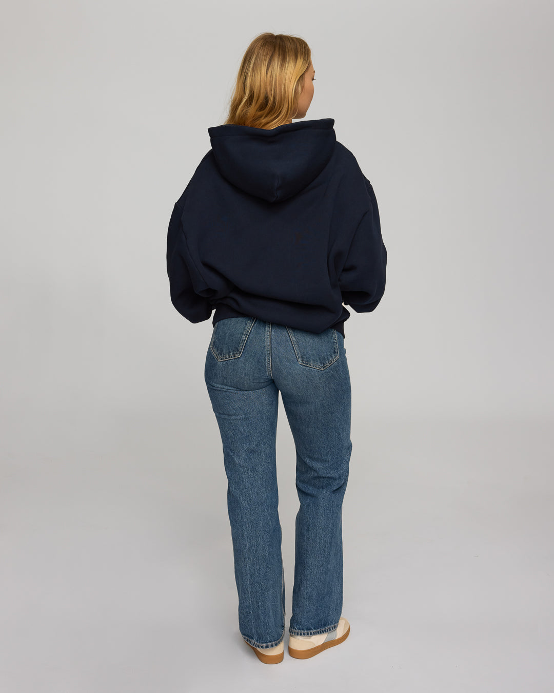 Person wearing a navy hoodie and blue jeans on a plain background