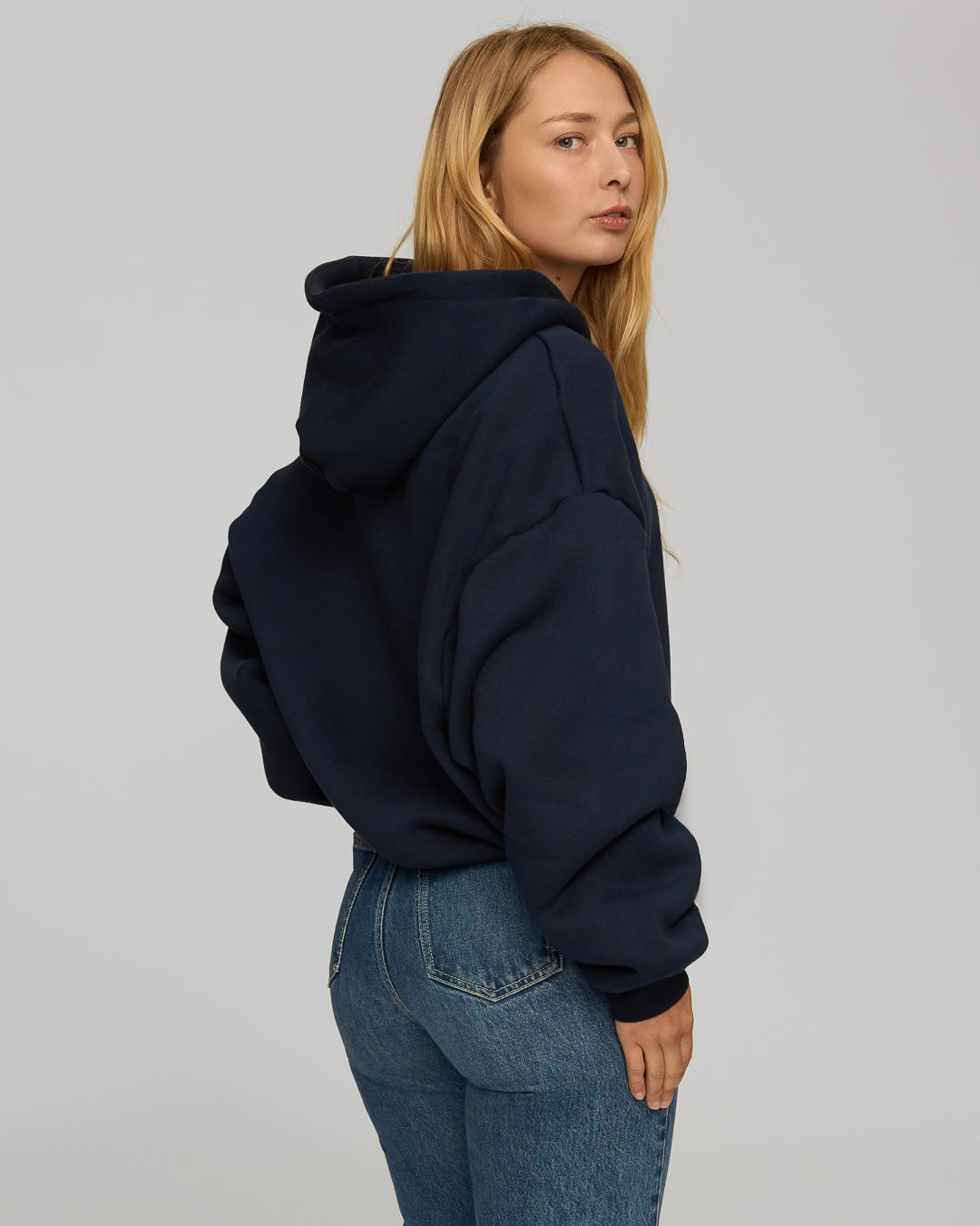 Person wearing a navy hoodie and blue jeans on a plain background