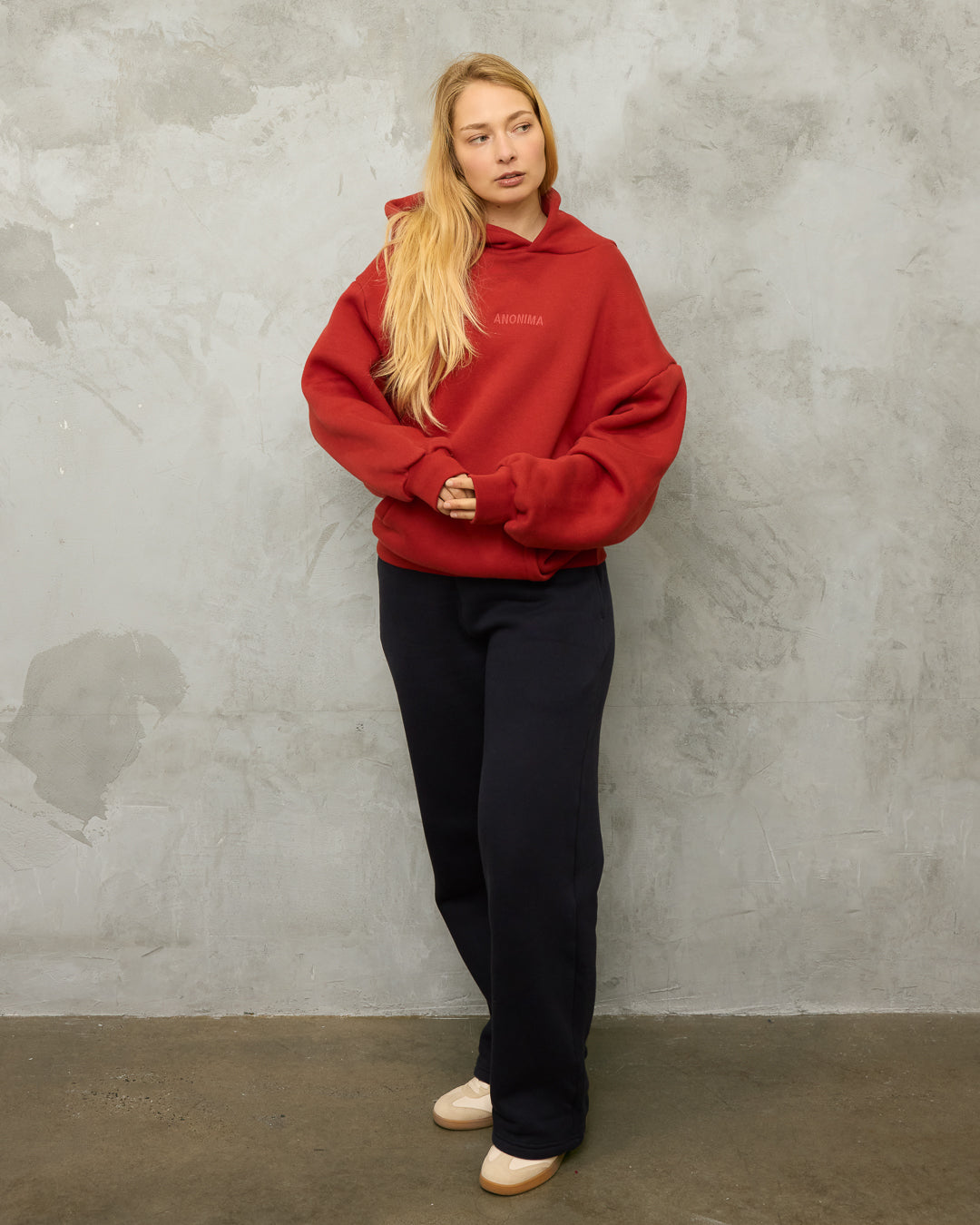 Person wearing a red hoodie and midnight blue track pants against a gray concrete wall.