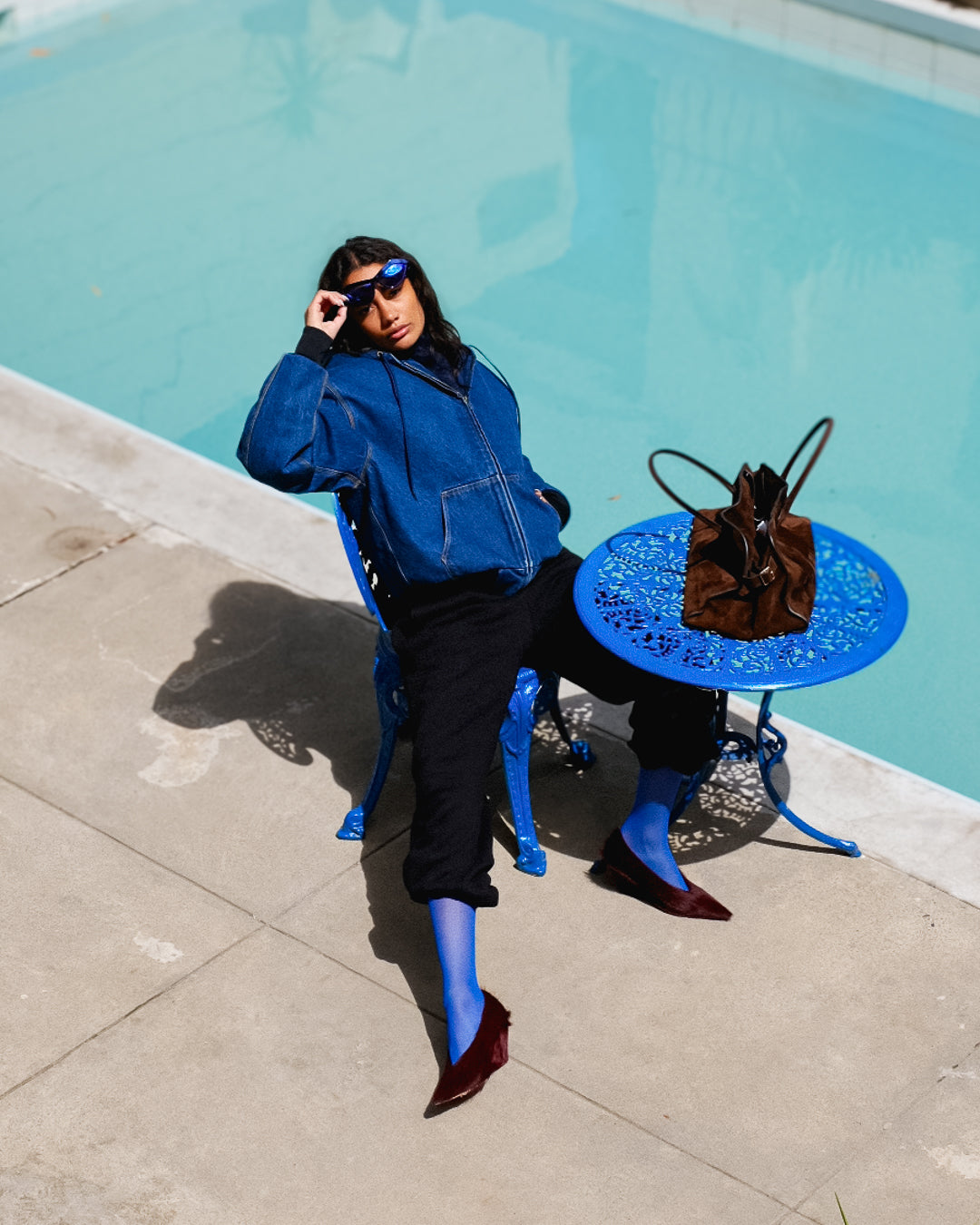 Person in blue outfit with sunglasses by a poolside