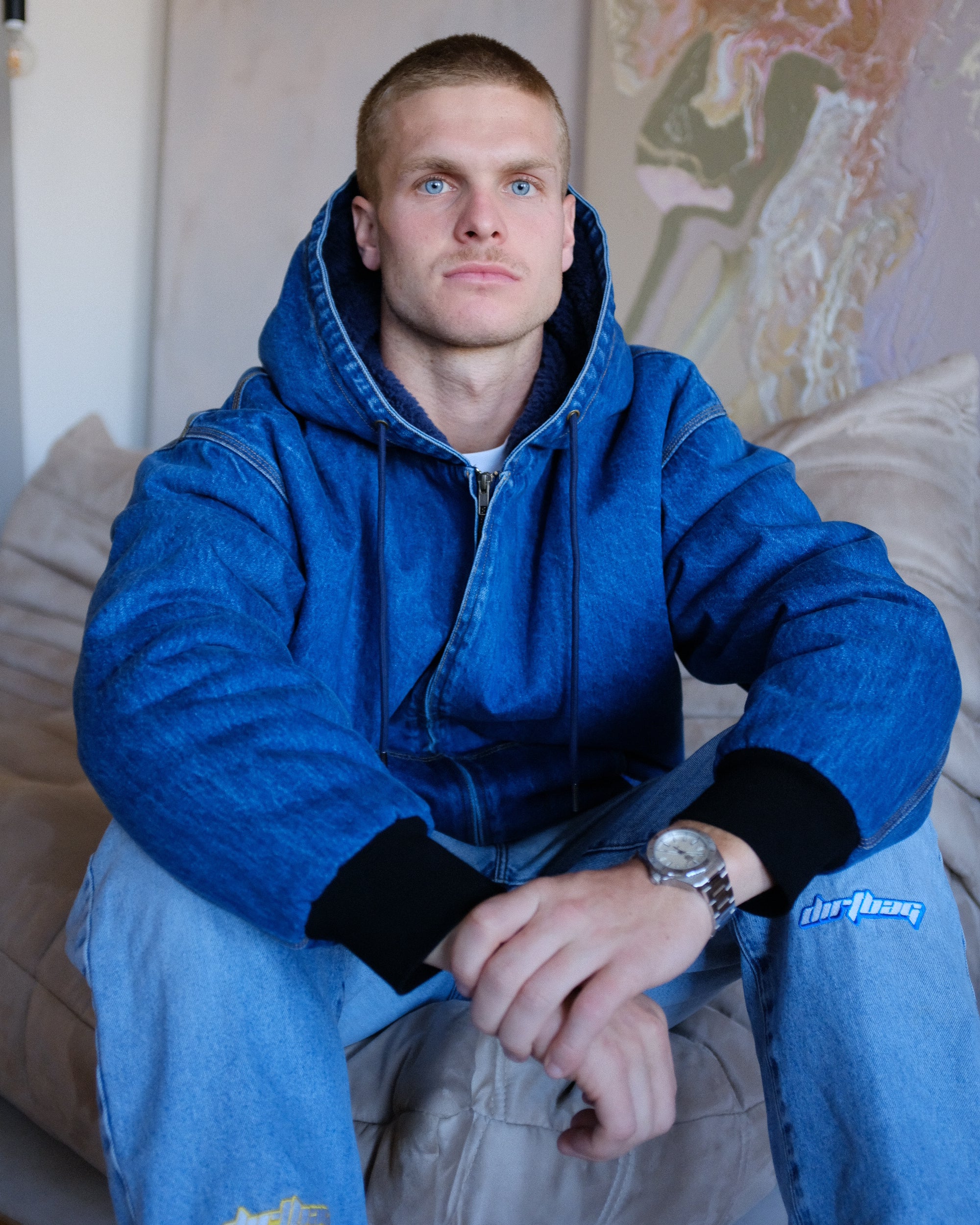 Man wearing a blue hoodie sitting on a couch with a neutral background