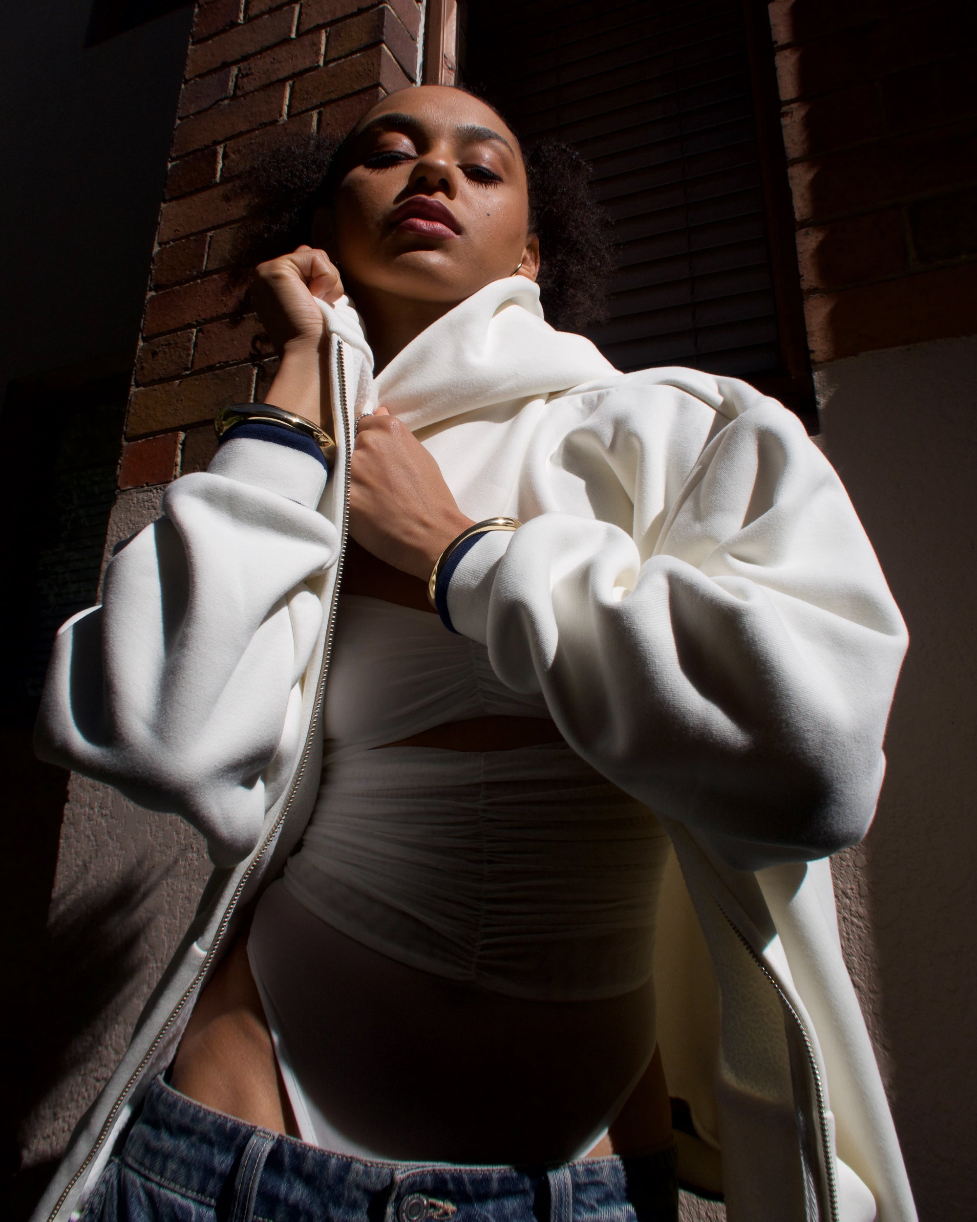 Person wearing a white hoodie and dark pants against a brick wall.