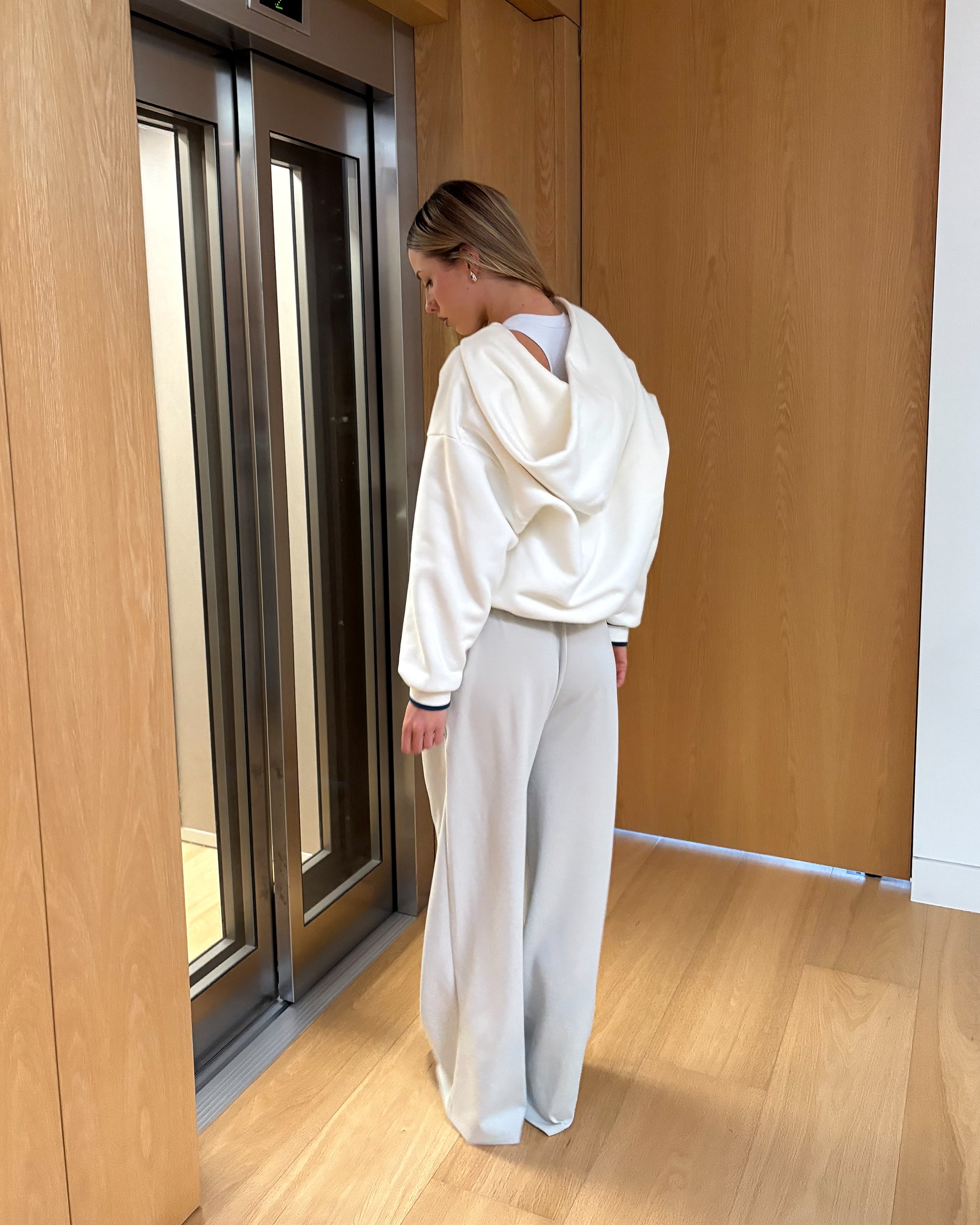 Person wearing a white outfit standing in front of a wooden door.
