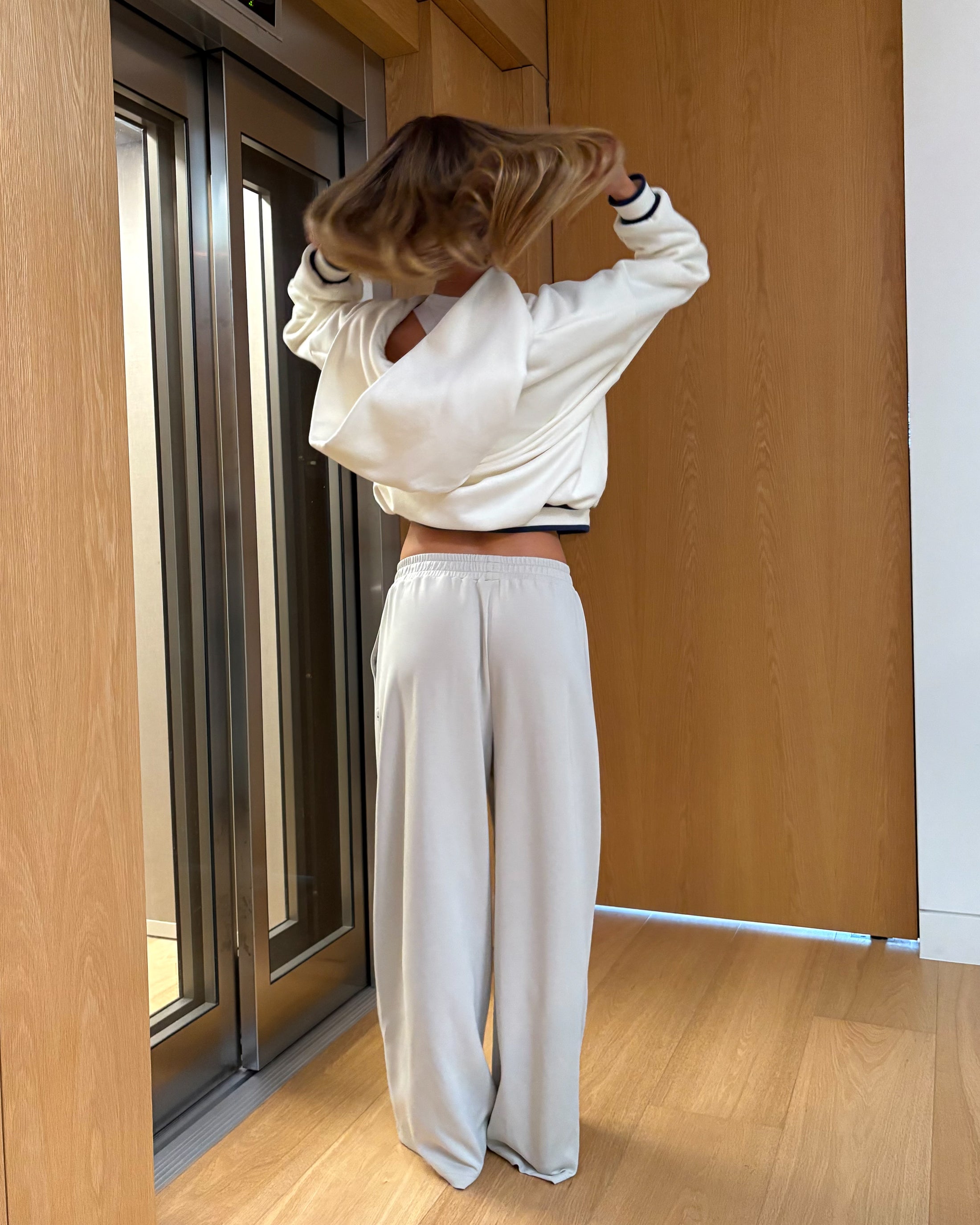 Person wearing a white sweatshirt and pants standing in a room with wooden walls and floor.