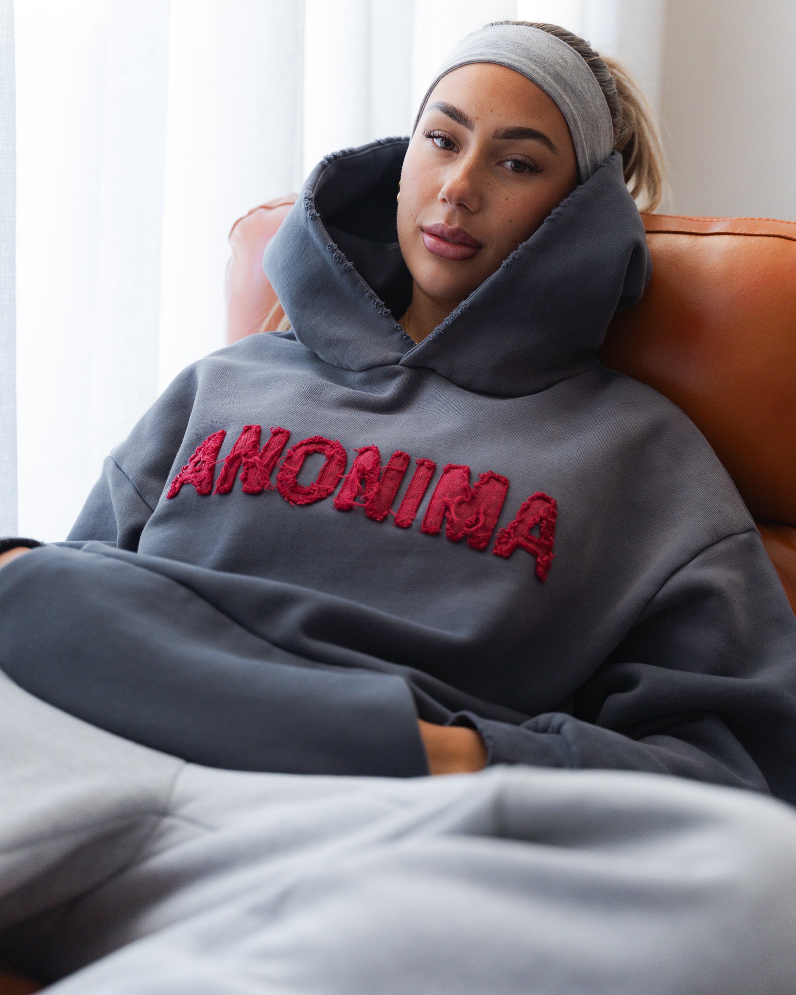 Person wearing a gray hoodie with 'ANOMIMA' text, sitting on a couch.
