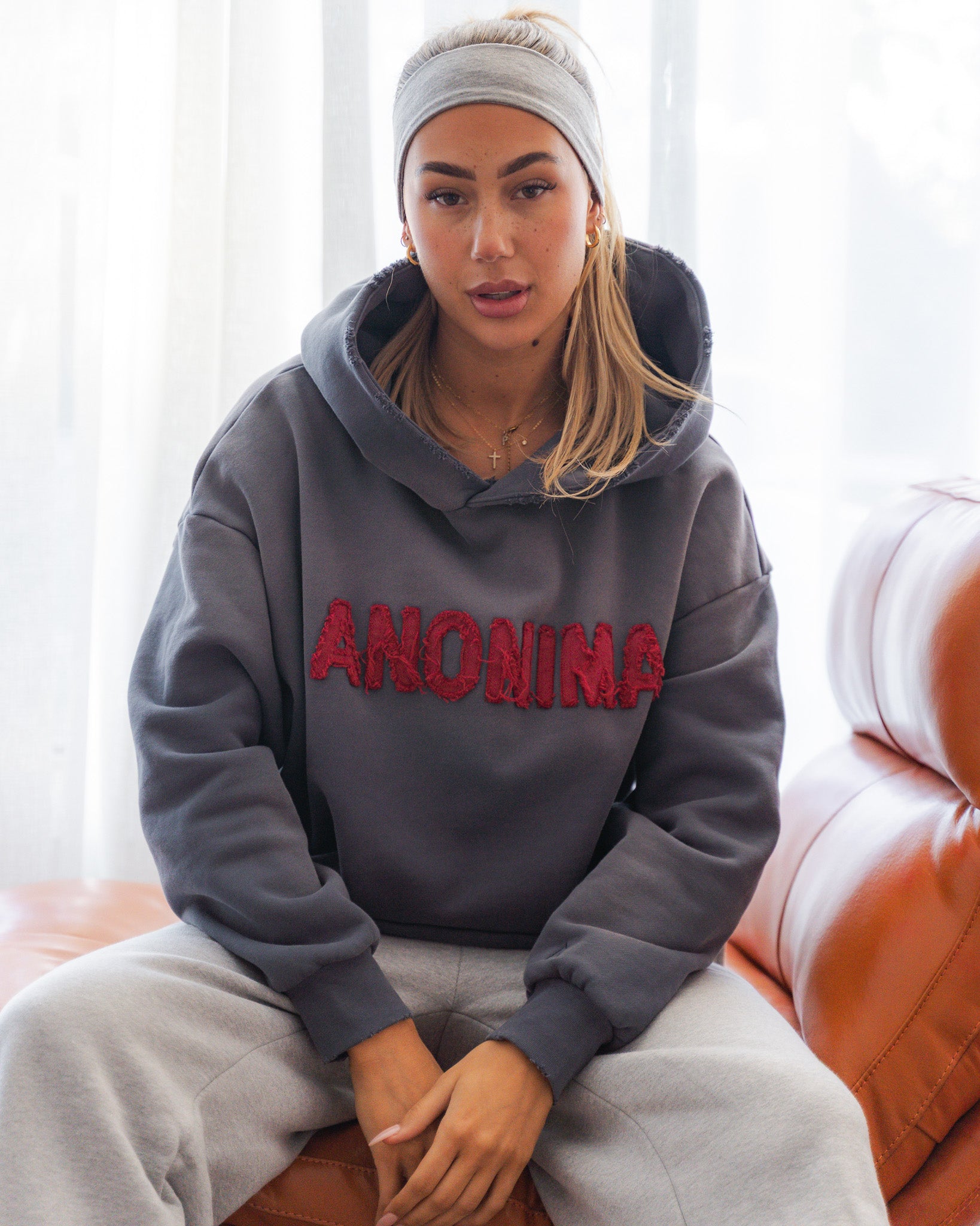 Person wearing a gray hoodie with 'ANONIMA' text, sitting on a couch.