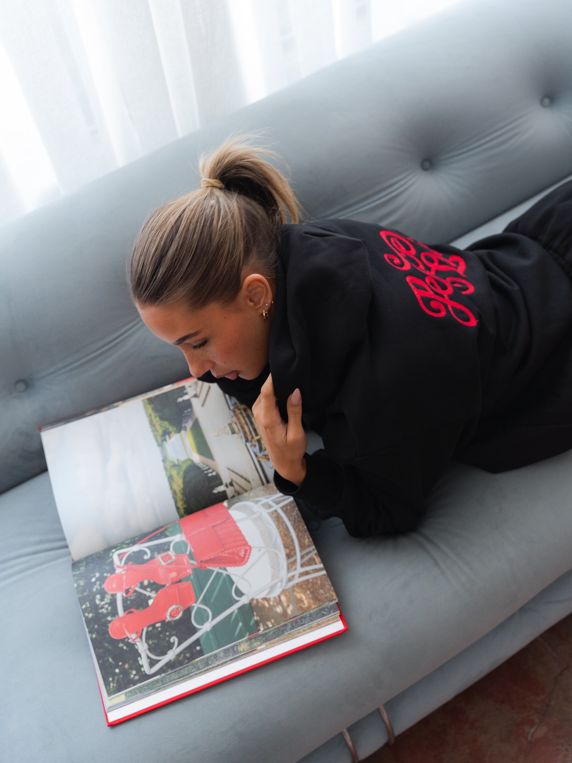 Woman reading a book on a gray couch with a white curtain in the background