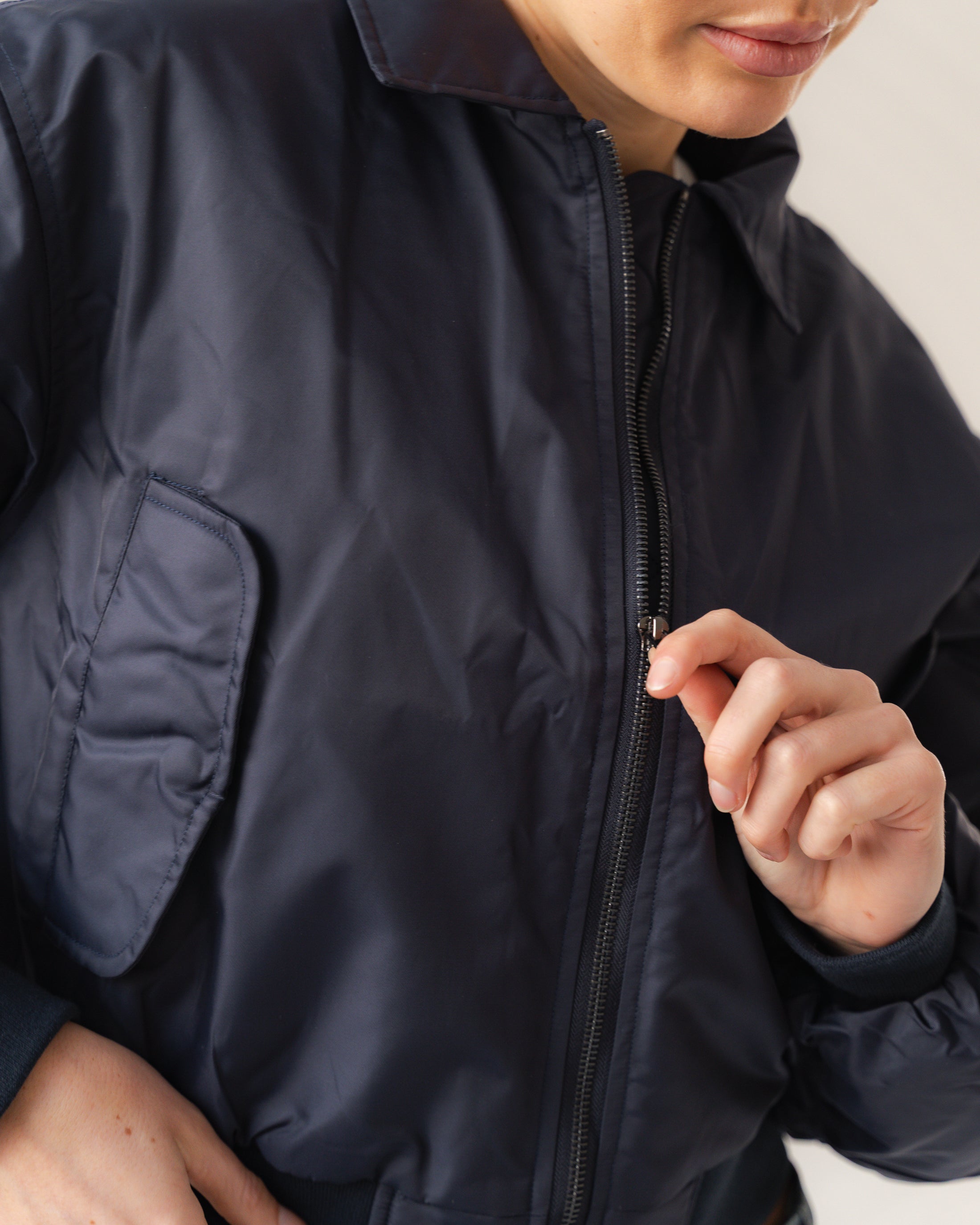 Person wearing a navy blue jacket with a close-up of the zipper.