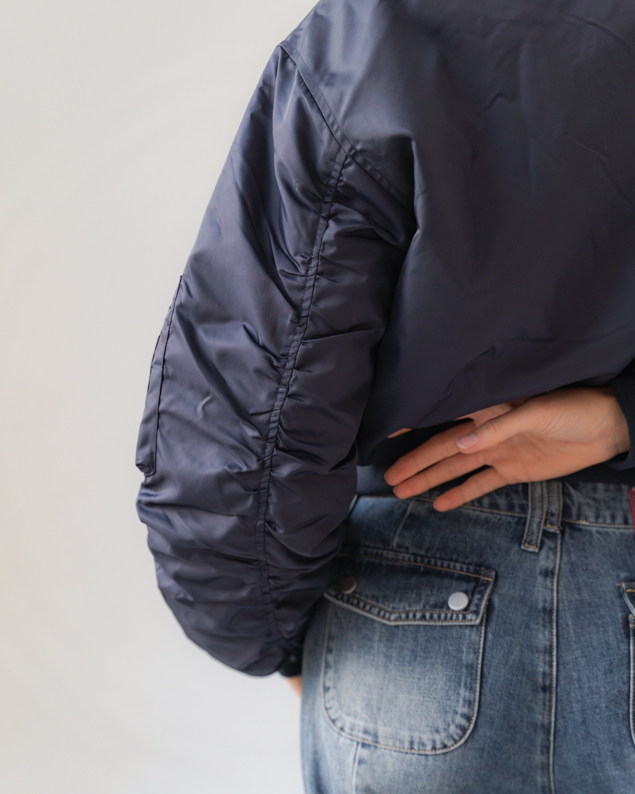 Person wearing a dark blue jacket and light blue jeans on a plain background
