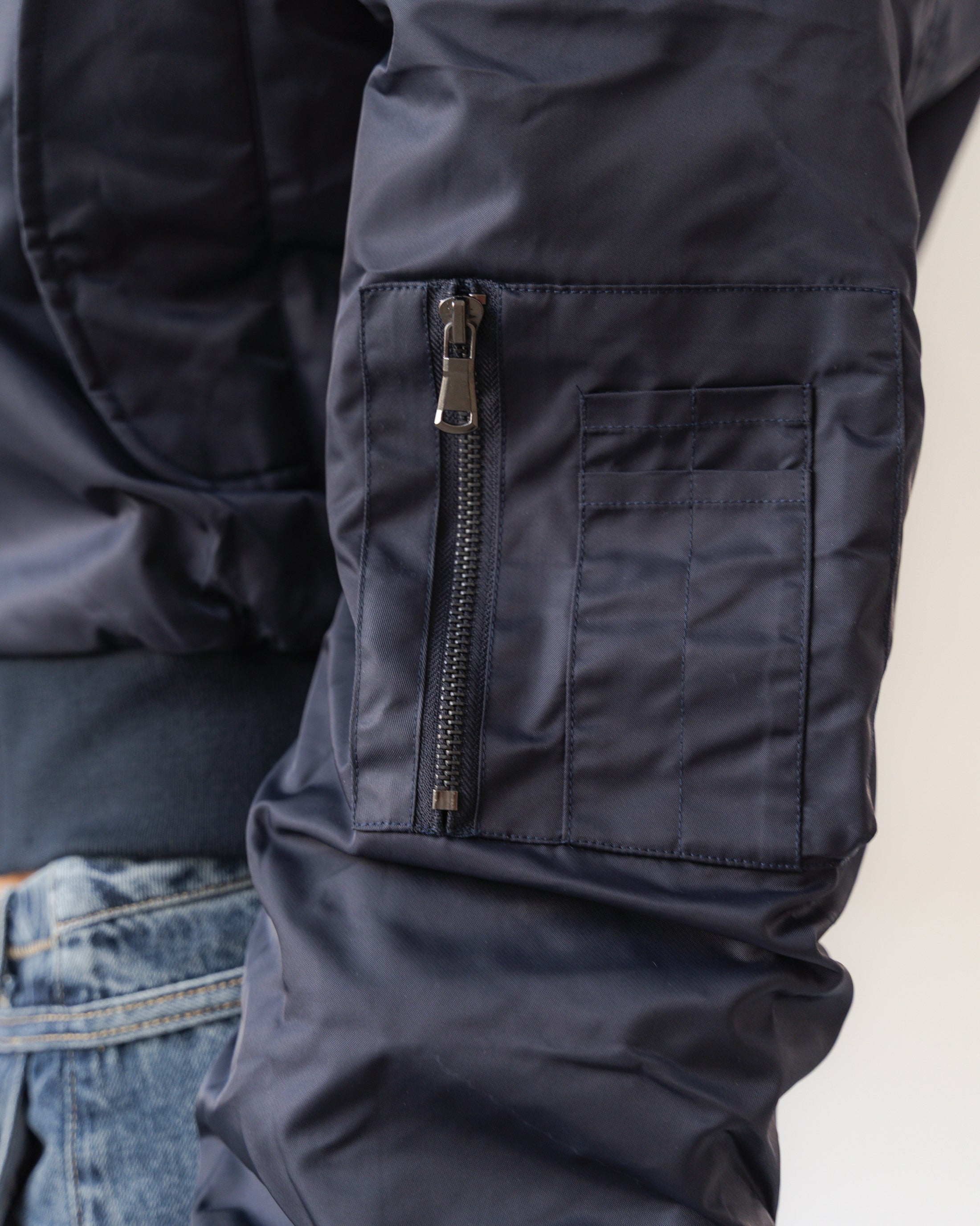 Close-up of a navy blue jacket with a zipper and pocket, worn over jeans.