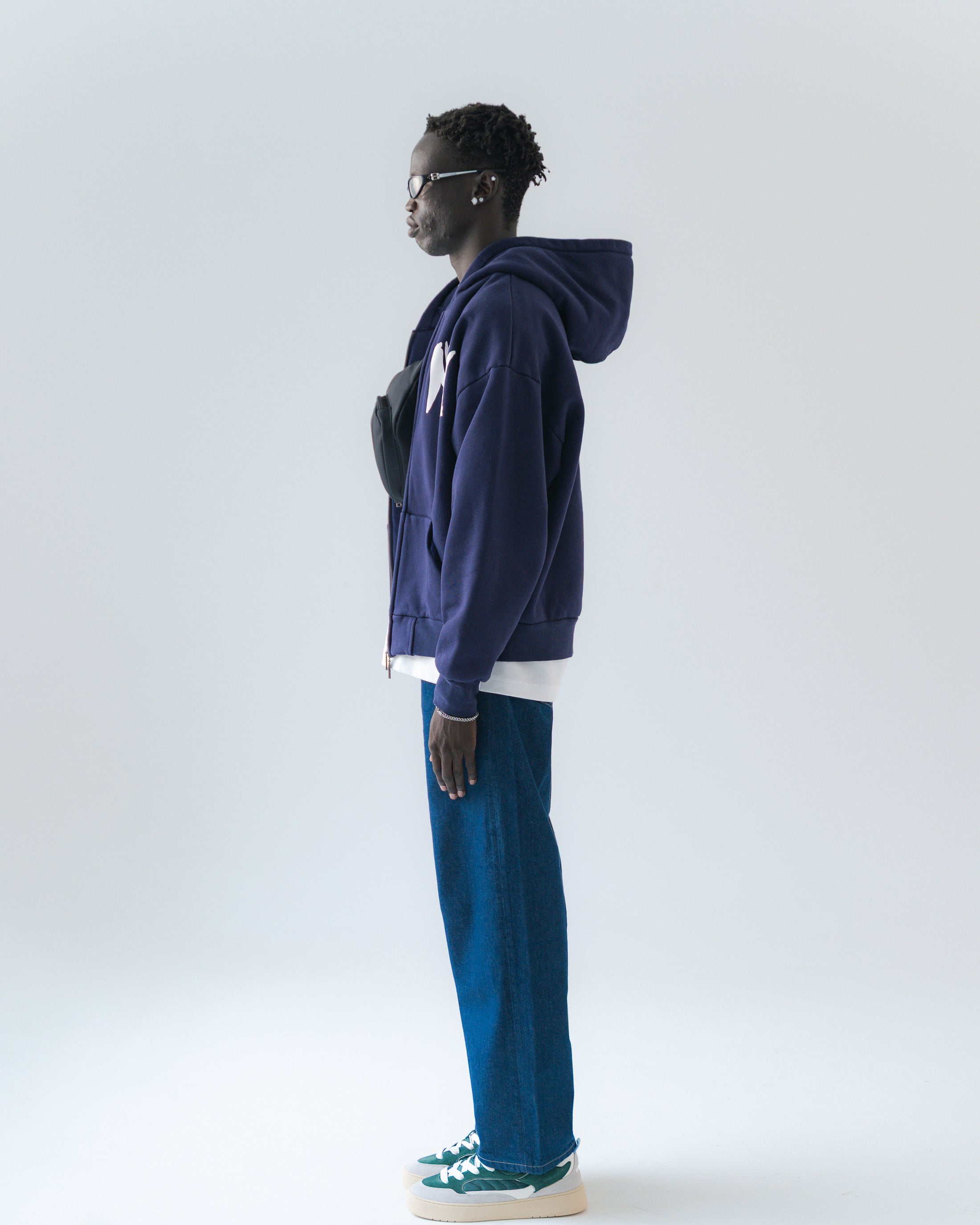 Person wearing a navy blue hoodie and blue pants on a white background