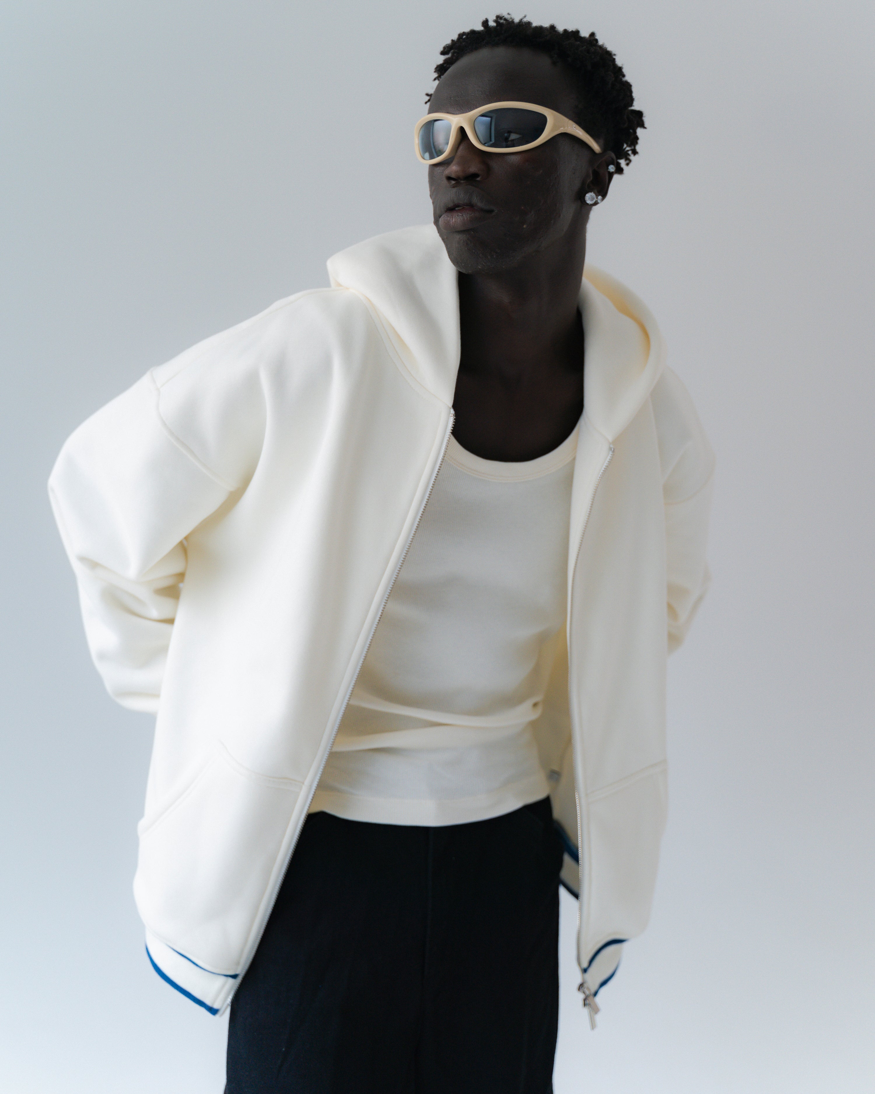 Person wearing a white jacket and sunglasses on a plain background