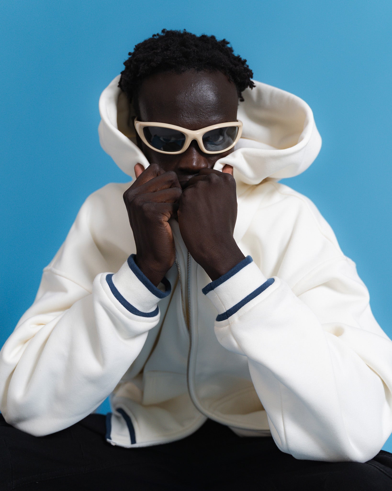 Person wearing a white hoodie and sunglasses against a blue background