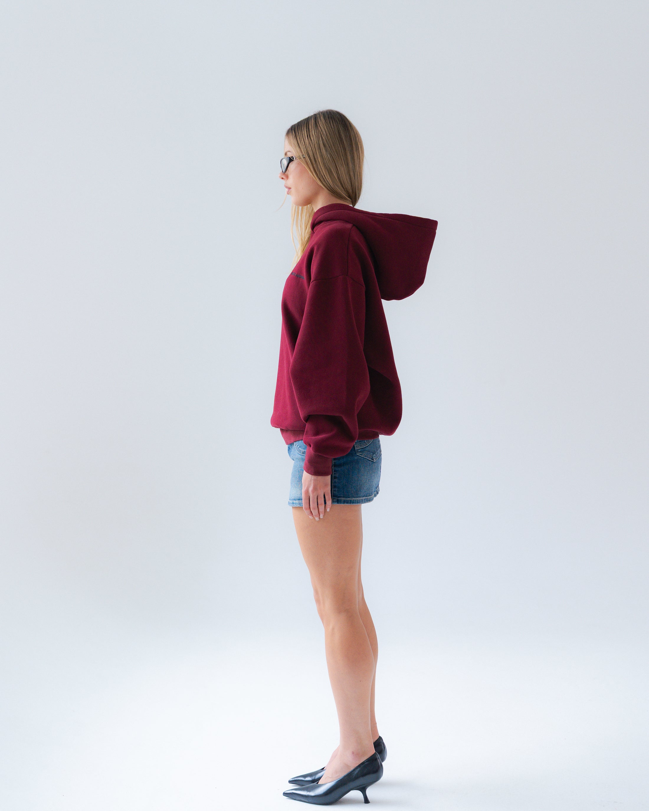 Woman wearing a burgundy hoodie and denim shorts on a white background
