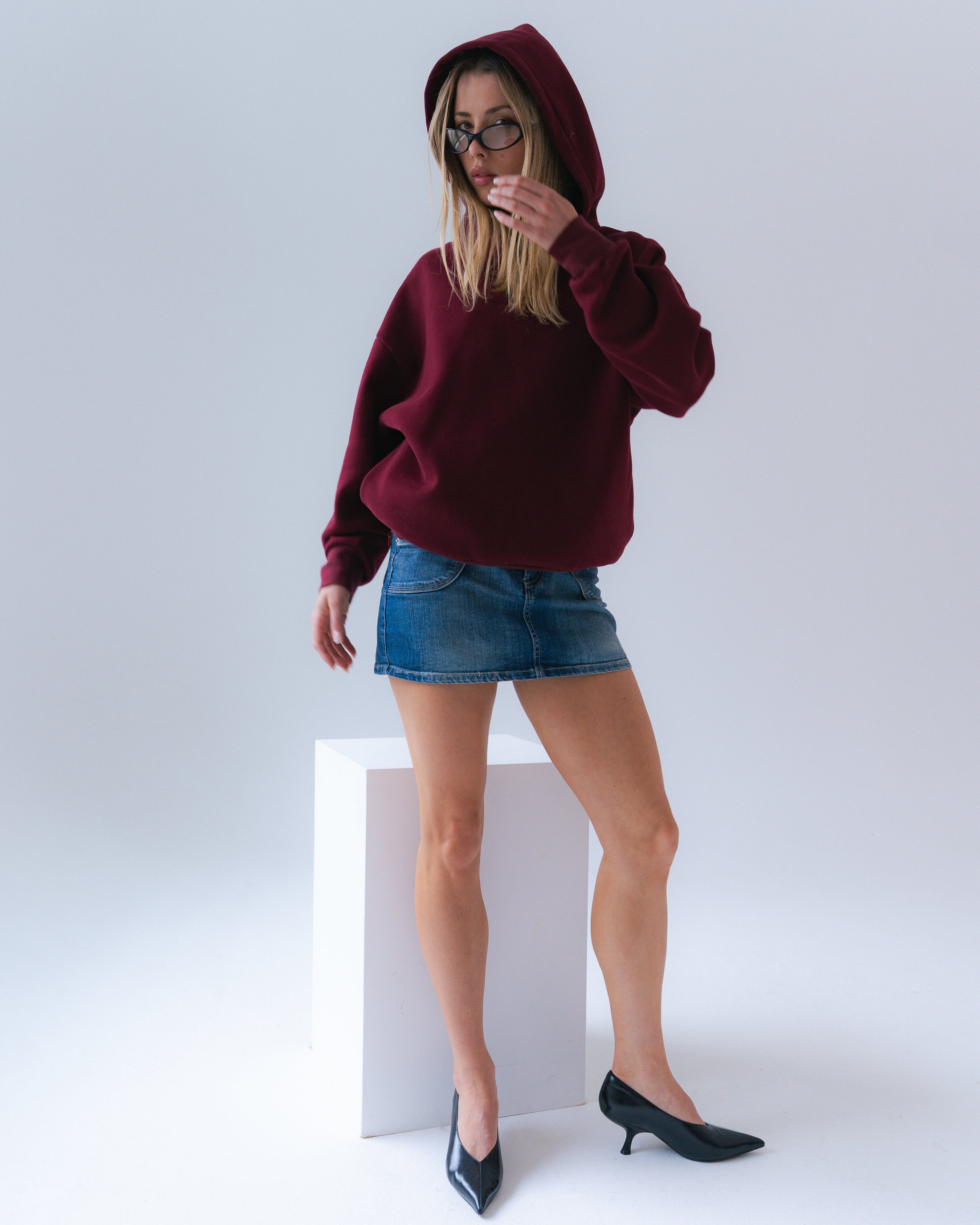 Person wearing a burgundy hoodie and denim skirt on a white background