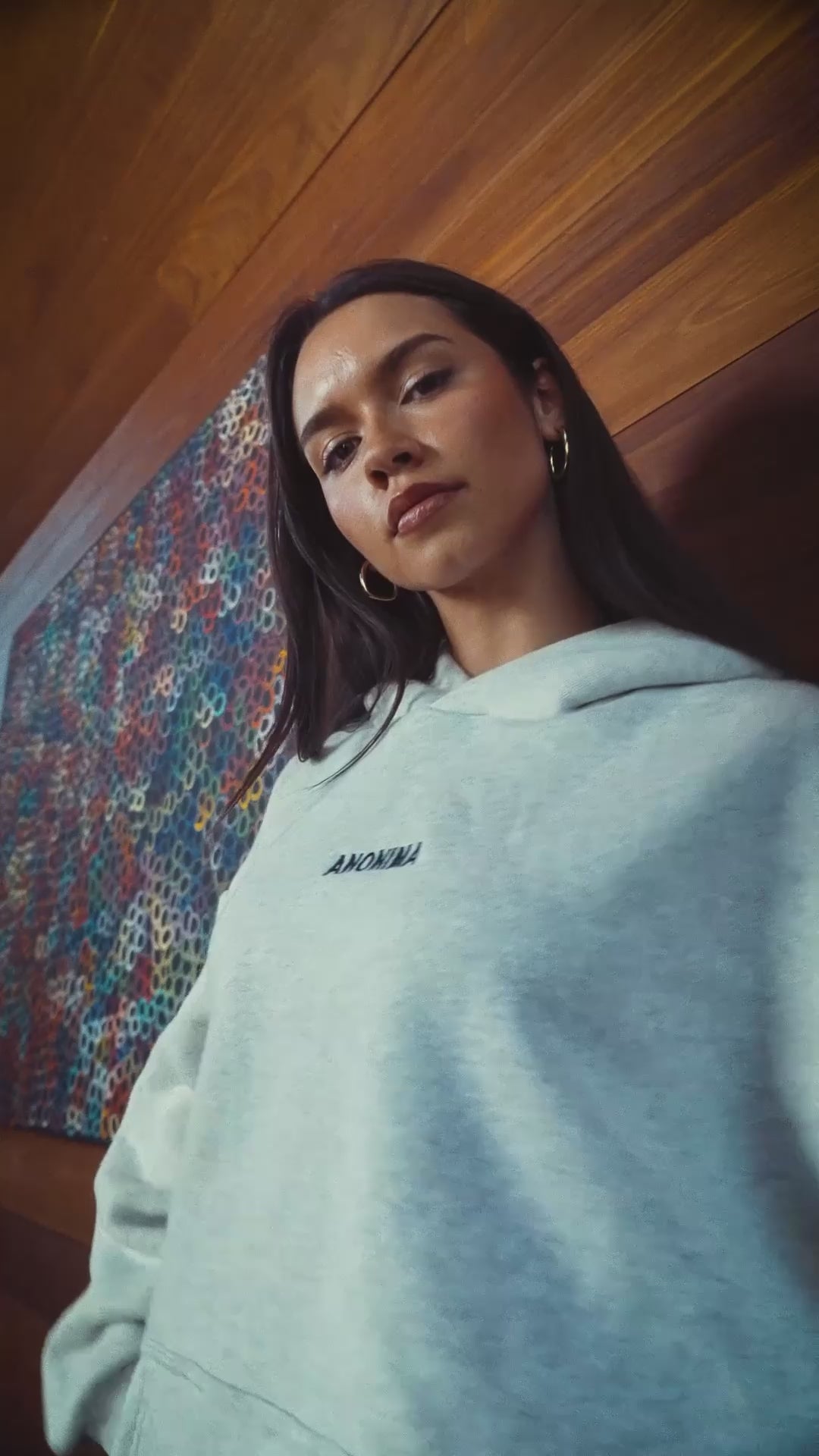 Woman wearing an ANONIMA Hoodie in front of timber lined wall