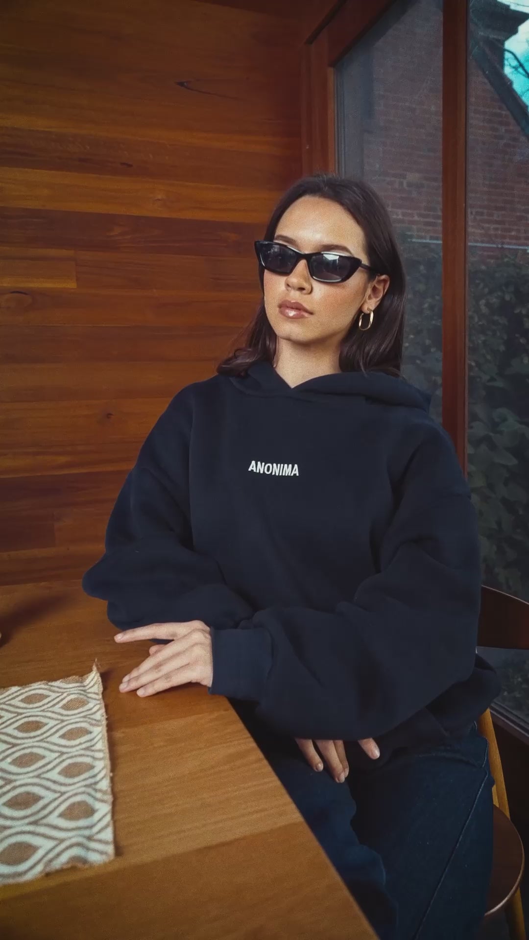 Woman wearing ANONIMA Hoodie in room with timber lined walls